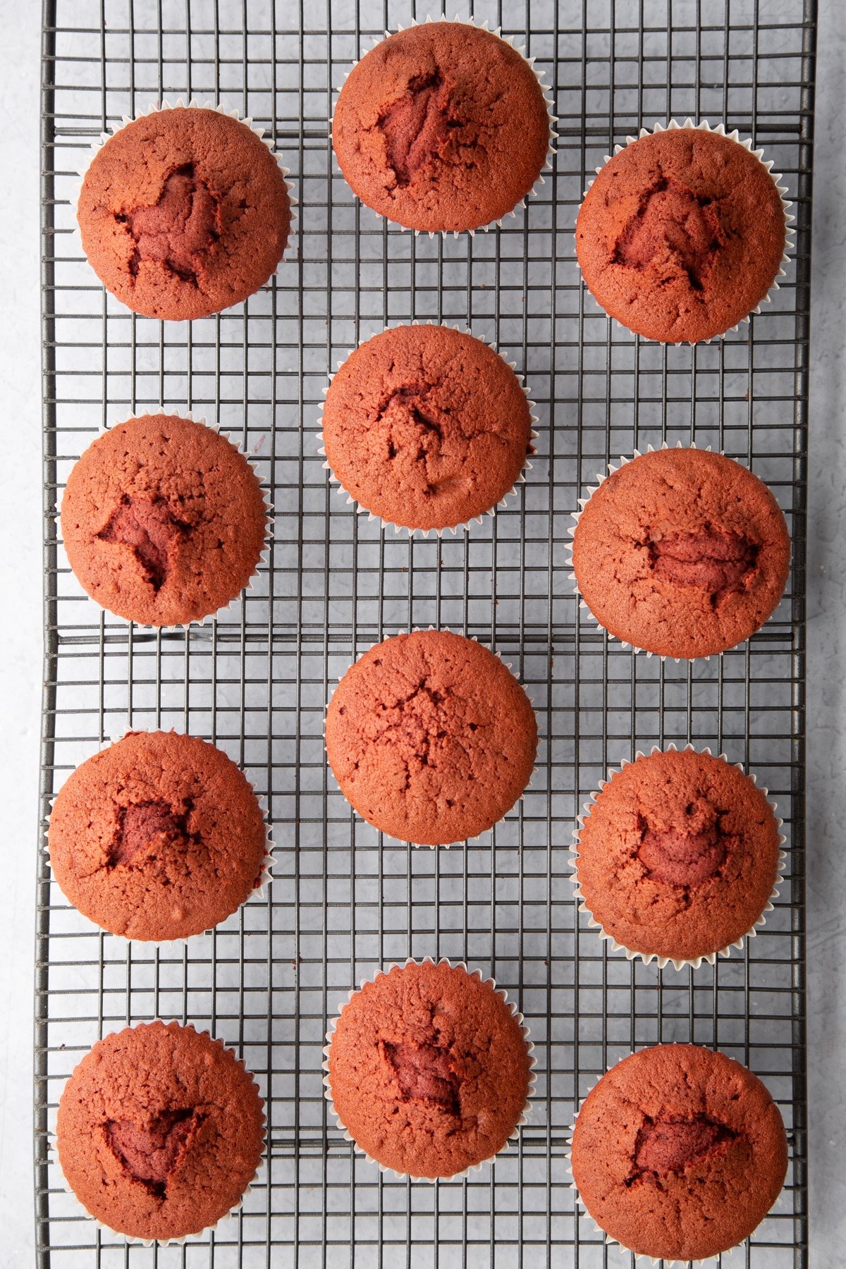 Red velvet cupcakes on a wire cooling rack. Ingredients to make red velvet Halloween cupcakes surround the tin.