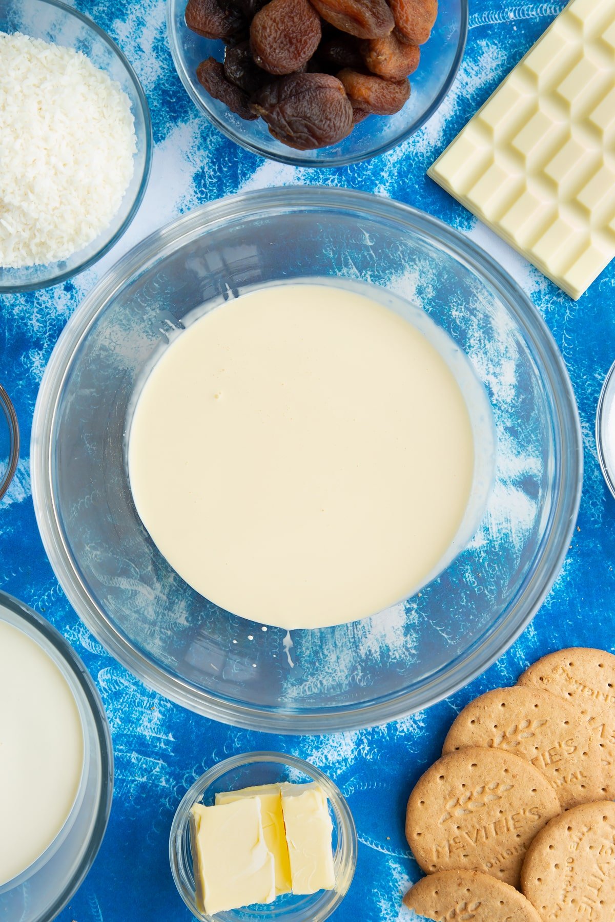 Double cream in a bowl. Ingredients to make an apricot cheesecake surround the bowl.