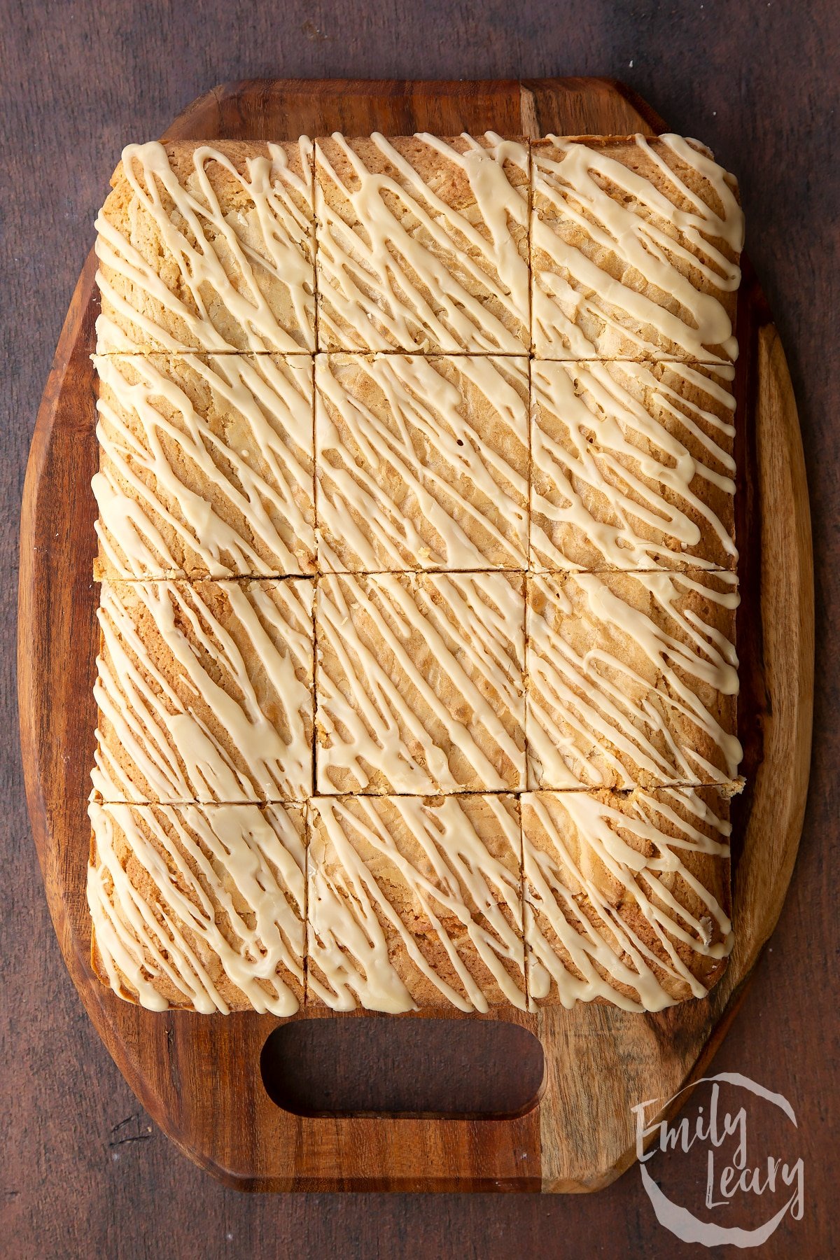 Freshly baked Baileys blondie drizzled with Baileys icing, cut into 12 pieces on a wooden board.