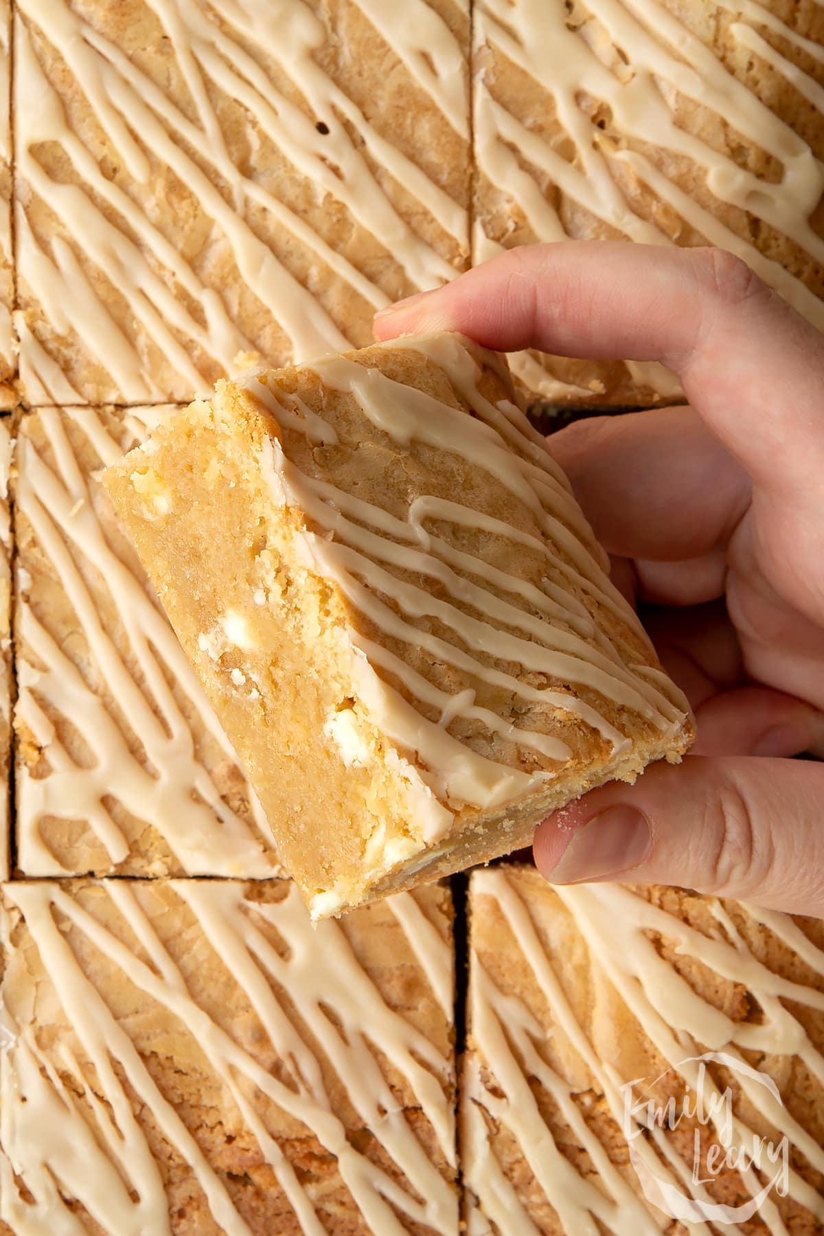 Hand holding a square of Baileys blondie above more blondies.