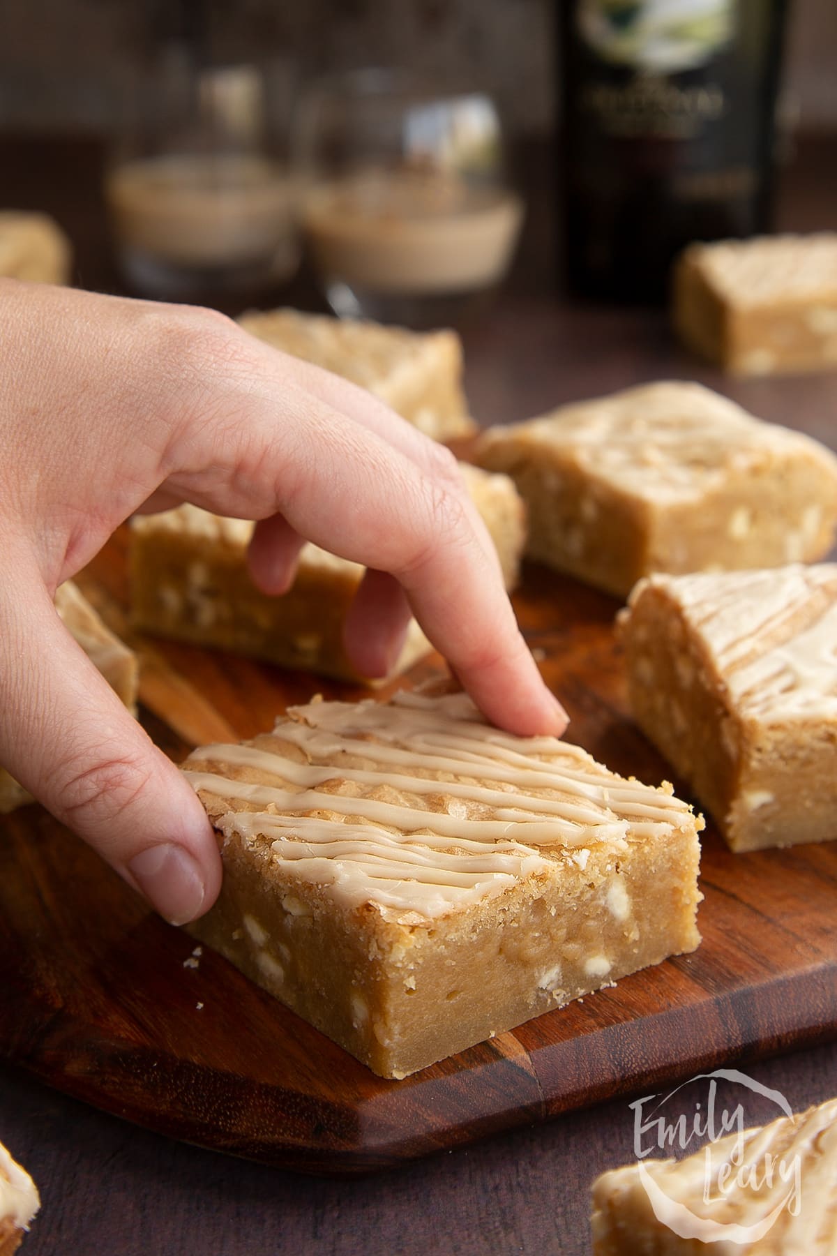Baileys blondies on a wooden board. A hand reaches for one.