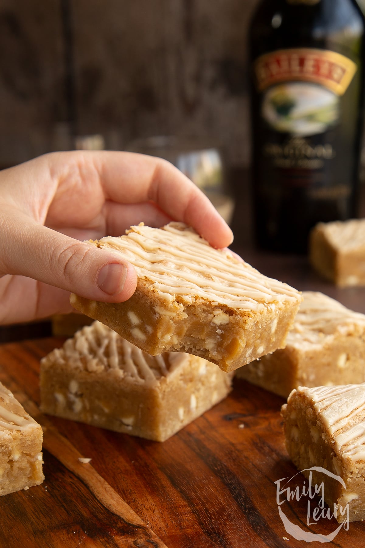 Baileys blondies on a wooden board. A hand holds one with a bite out of it.