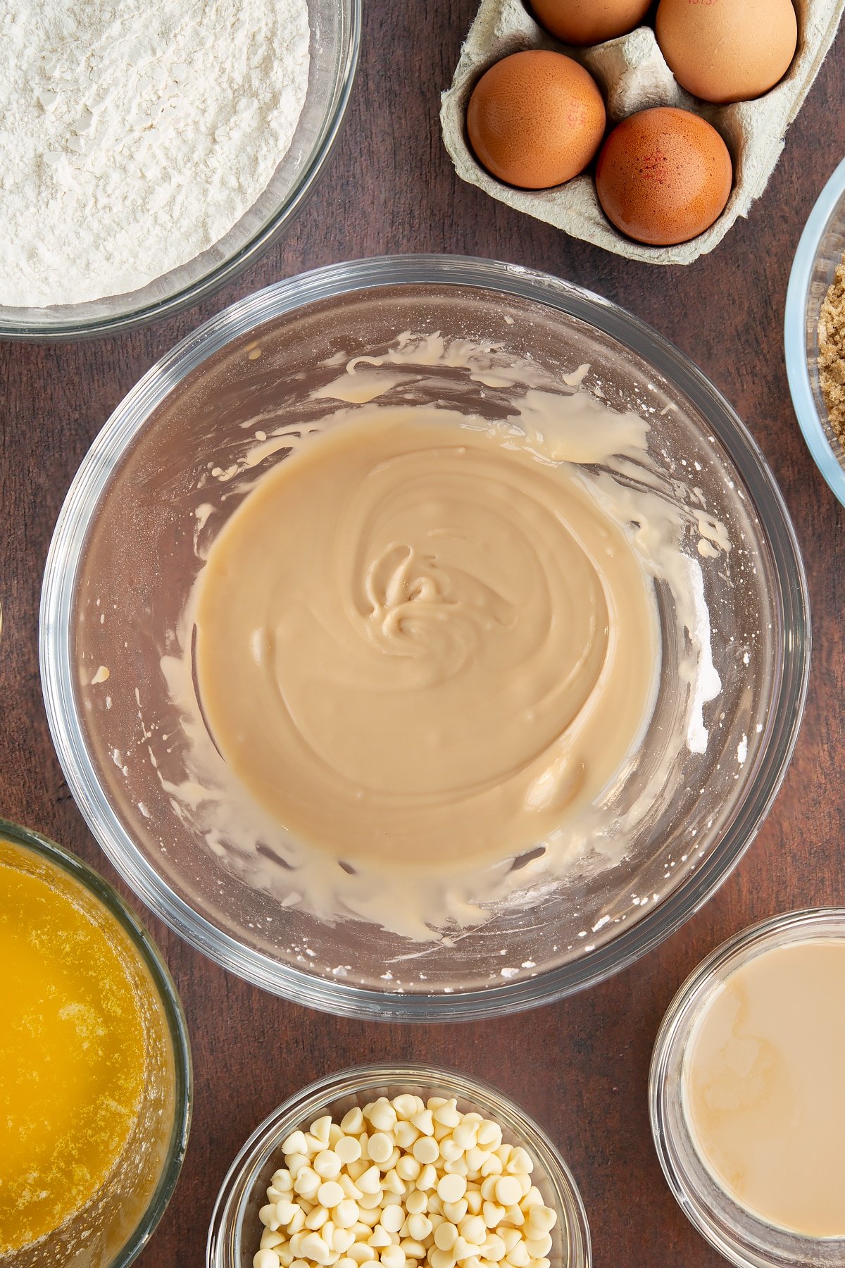 Baileys icing in a glass mixing bowl. Ingredients to make Baileys blondies surround the bowl.