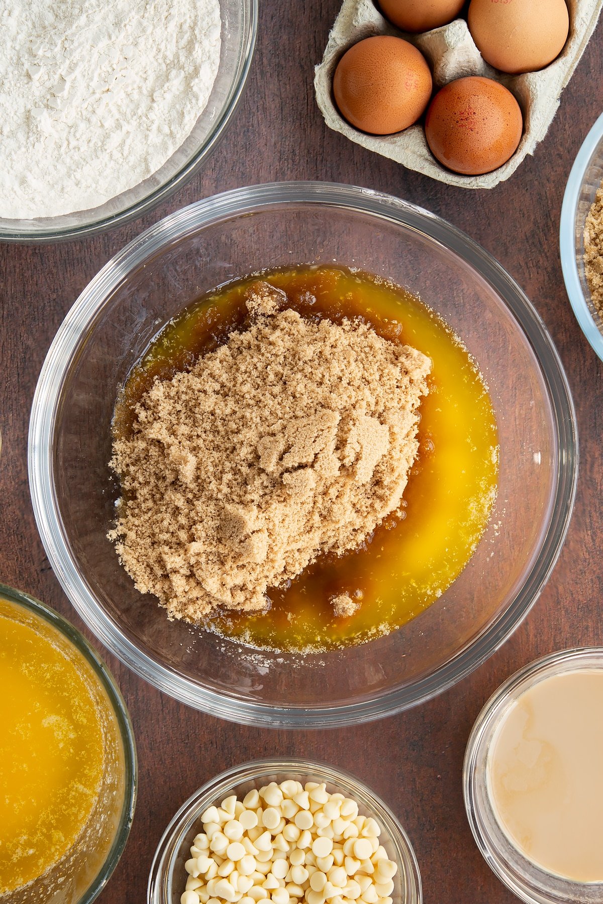 Melted butter and soft brown sugar in a glass mixing bowl. Ingredients to make Baileys blondies surround the bowl.