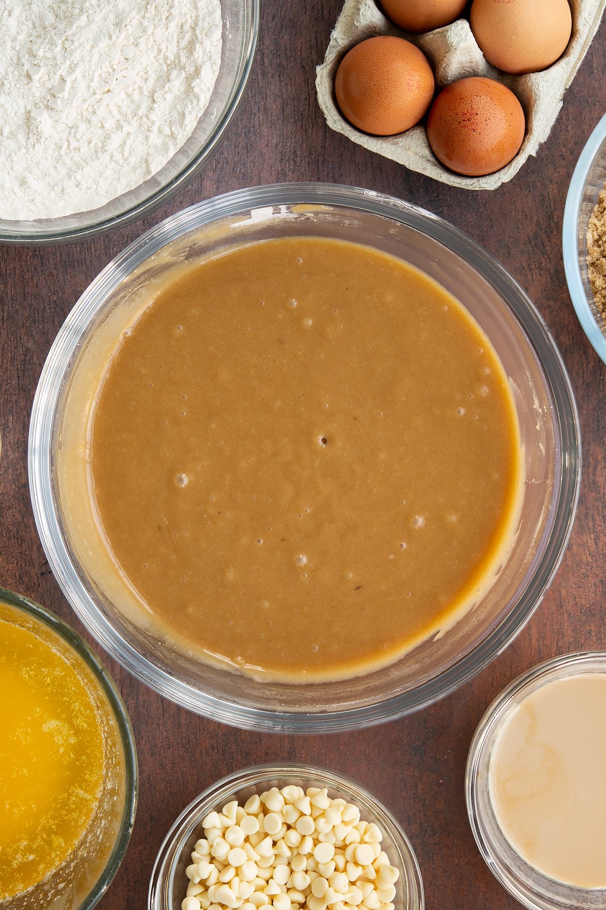 Baileys blondie batter in a glass mixing bowl. Ingredients to make Baileys blondies surround the bowl.