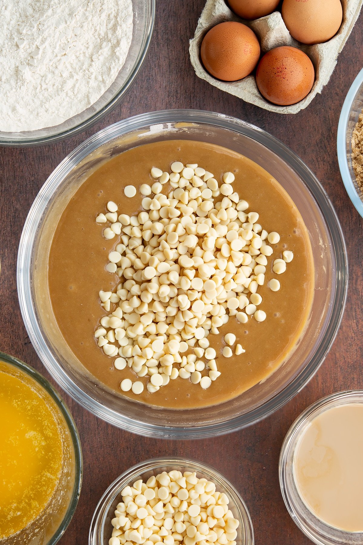 Baileys blondie batter in a glass mixing bowl with white chocolate chips on top. Ingredients to make Baileys blondies surround the bowl.