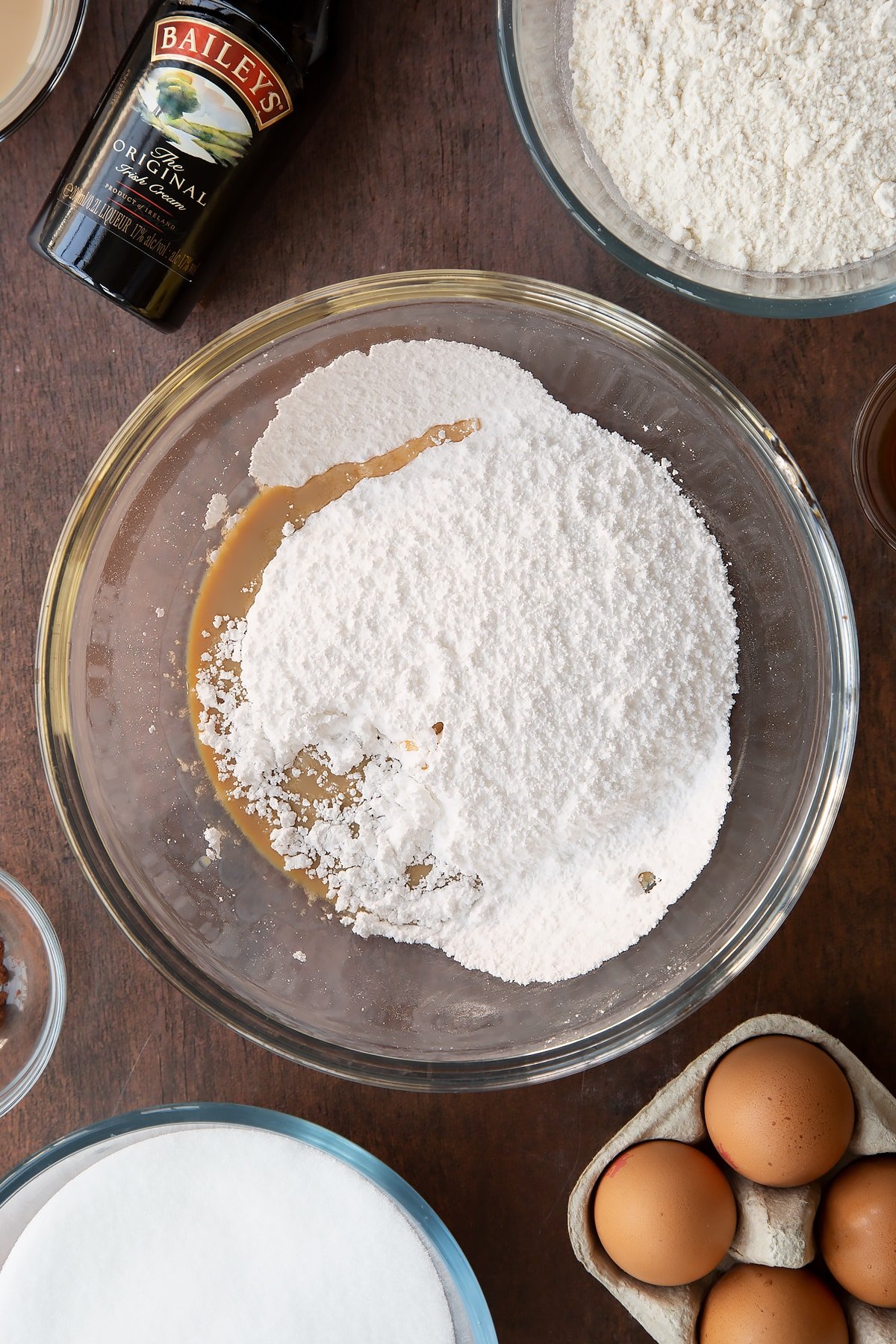 Icing sugar and Baileys in a bowl. Ingredients to make Baileys brownies surround the bowl.