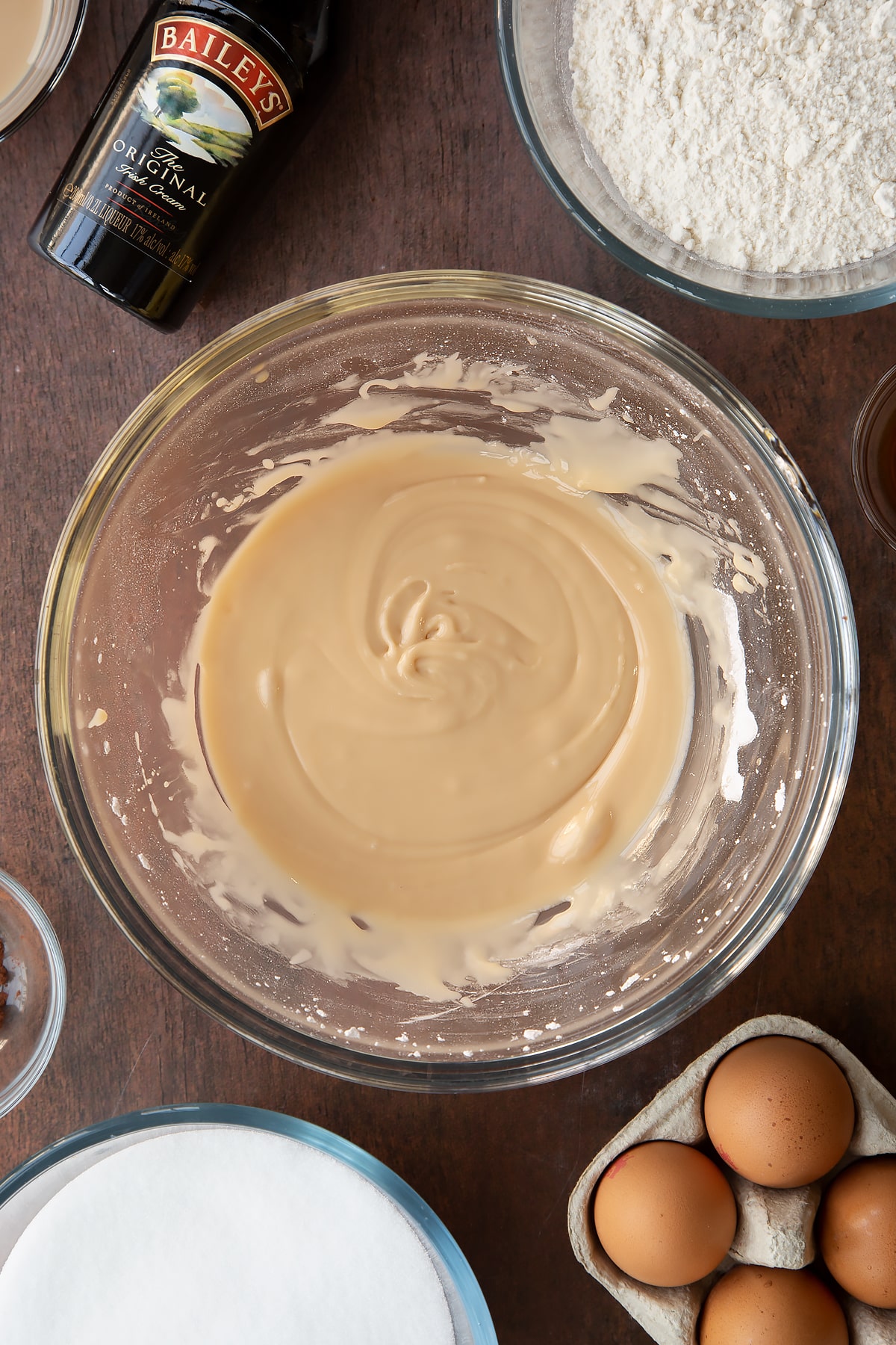 Baileys icing in a bowl. Ingredients to make Baileys brownies surround the bowl.