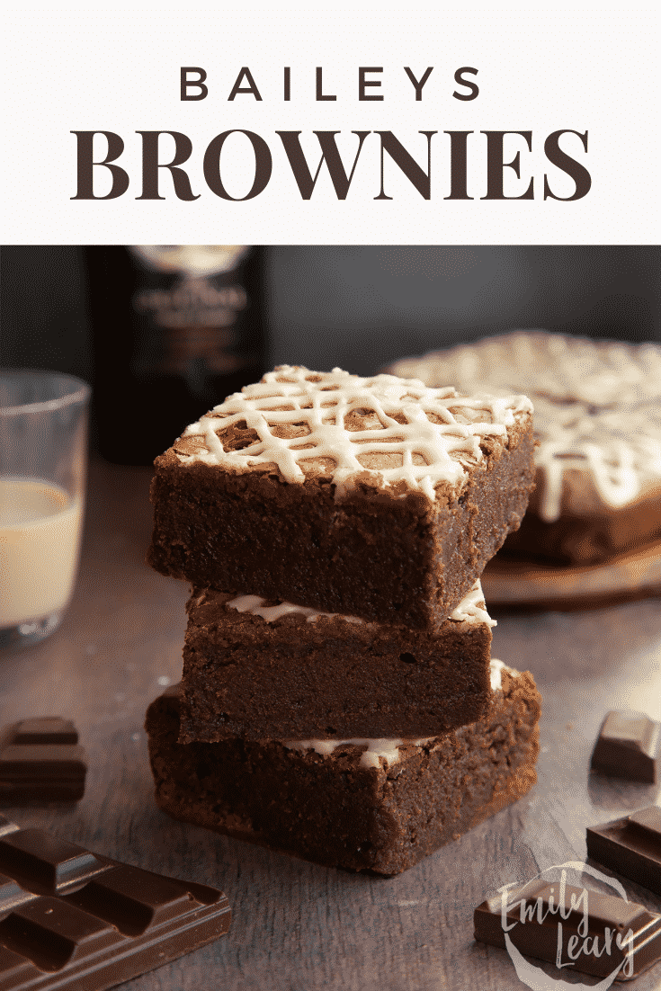 A stack of iced Baileys brownies, with more brownies and a bottle of Baileys in the background. Caption reads: Baileys brownies.