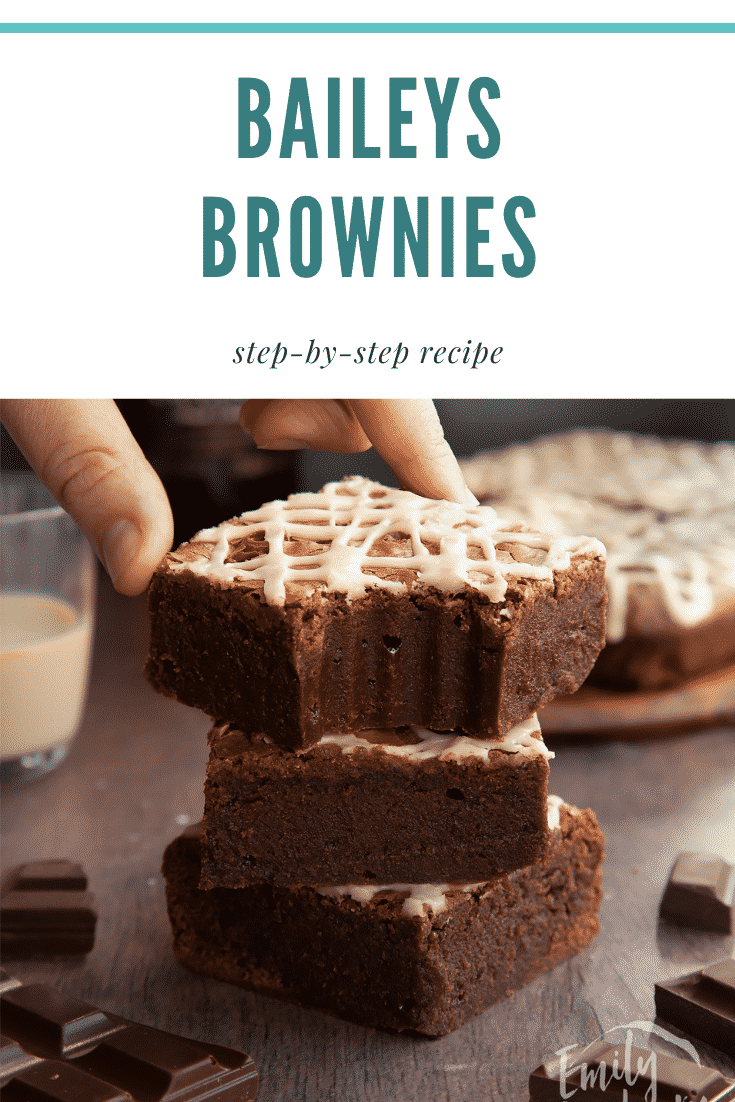 Stack of iced Baileys brownies, with more brownies and a bottle of Baileys in the background. A hand reaches for one with a bite out of it. Caption reads: Baileys brownies. Step-by-step recipe.