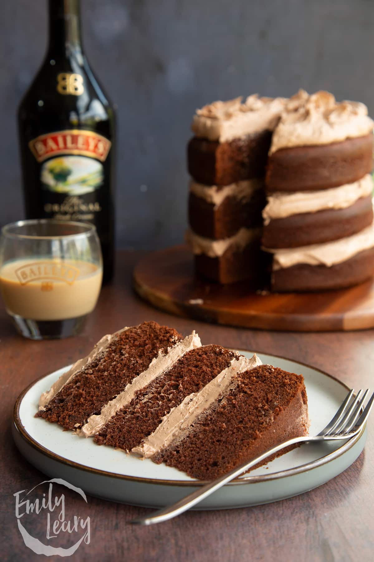 Slice of chocolate Baileys cake with Baileys buttercream frosting on a white plate with a fork.