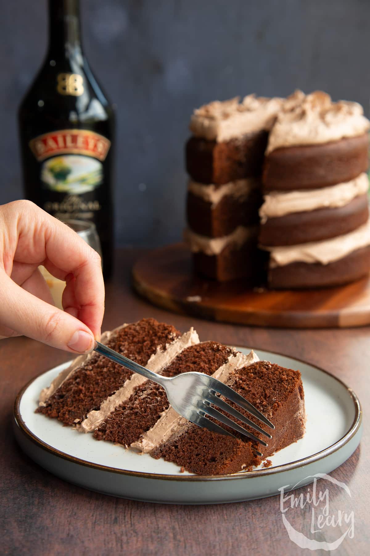 Slice of chocolate Baileys cake with Baileys buttercream frosting on a white plate with a fork delving into it