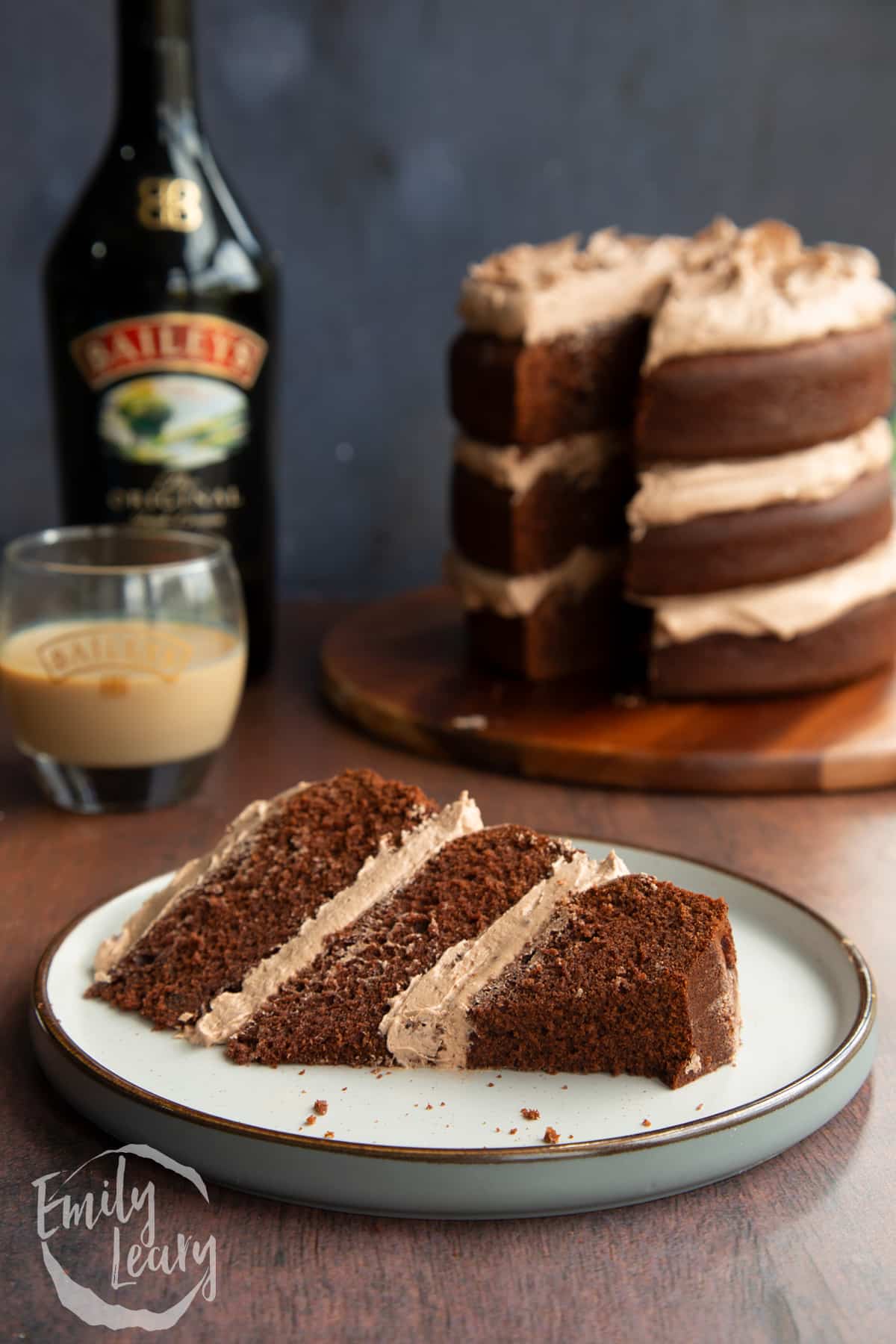 Slice of chocolate Baileys cake with Baileys buttercream frosting on a white plate with a piece cut away.