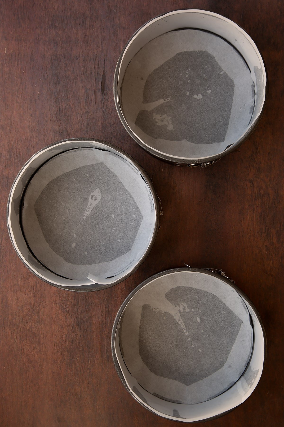 Three lined cake tins on a dark wooden surface.