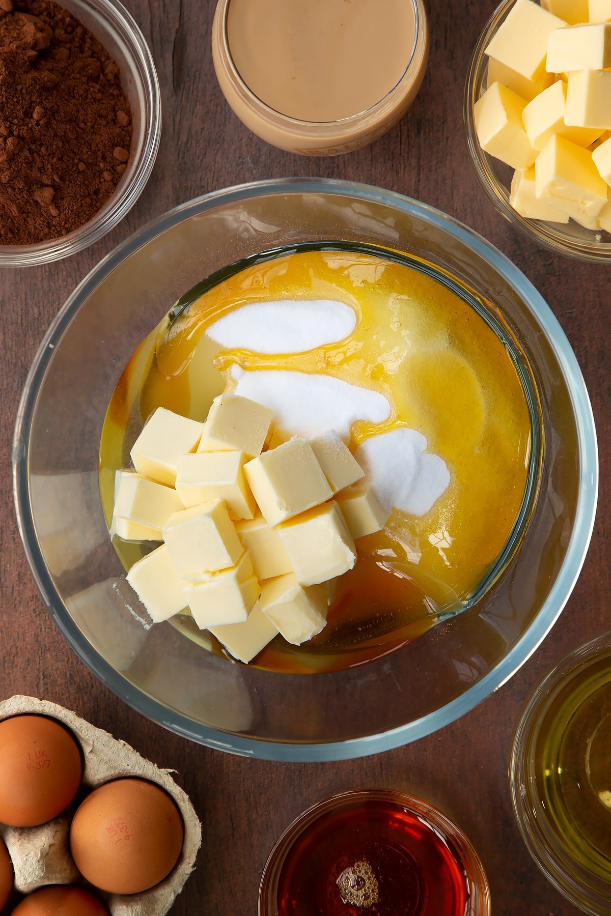 Butter, vegetable oil, caster sugar and golden syrup in a glass mixing bowl. Ingredients to make a Baileys cake surround the bowl.