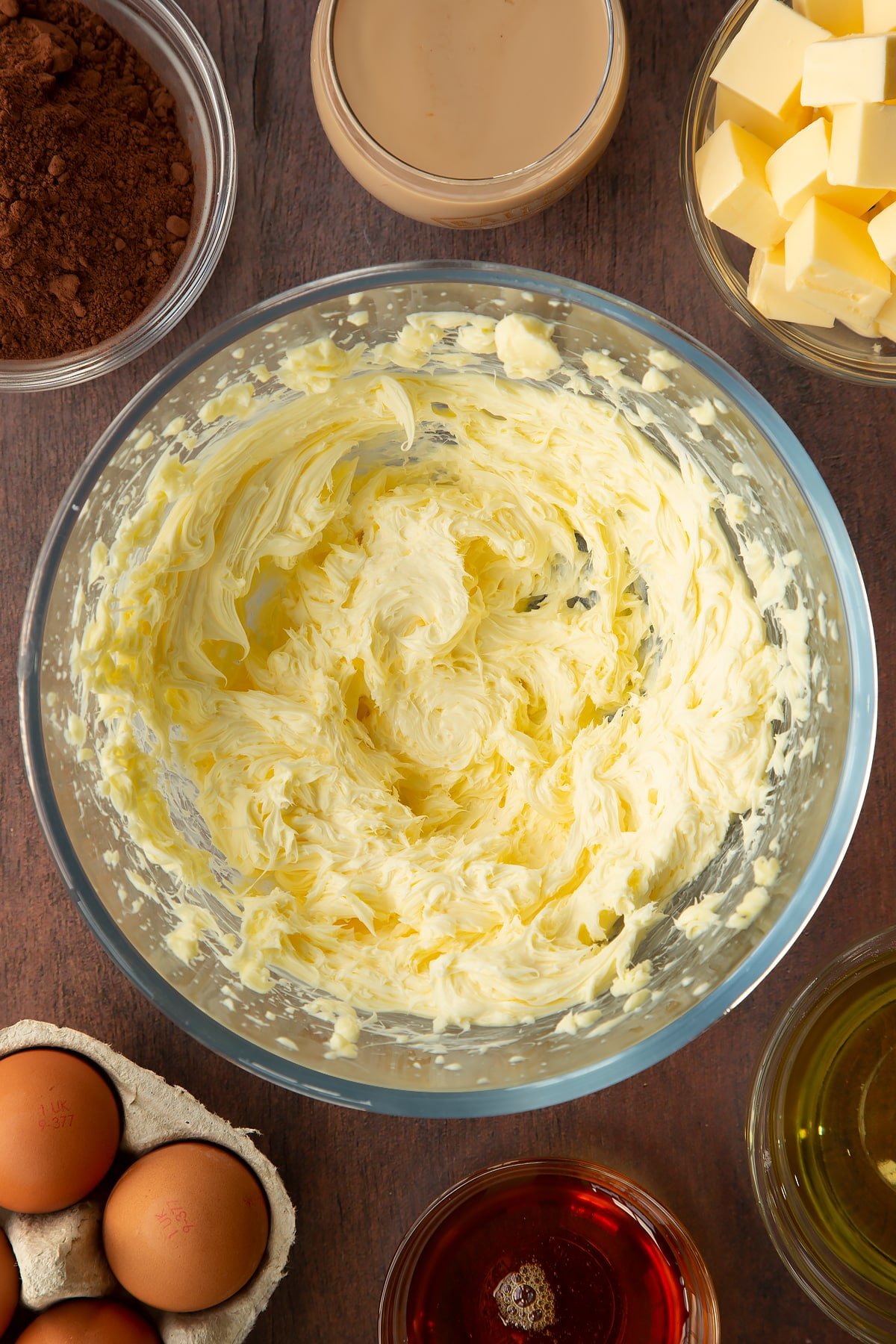 Whipped butter in a glass mixing bowl. Ingredients to make a Baileys cake surround the bowl.