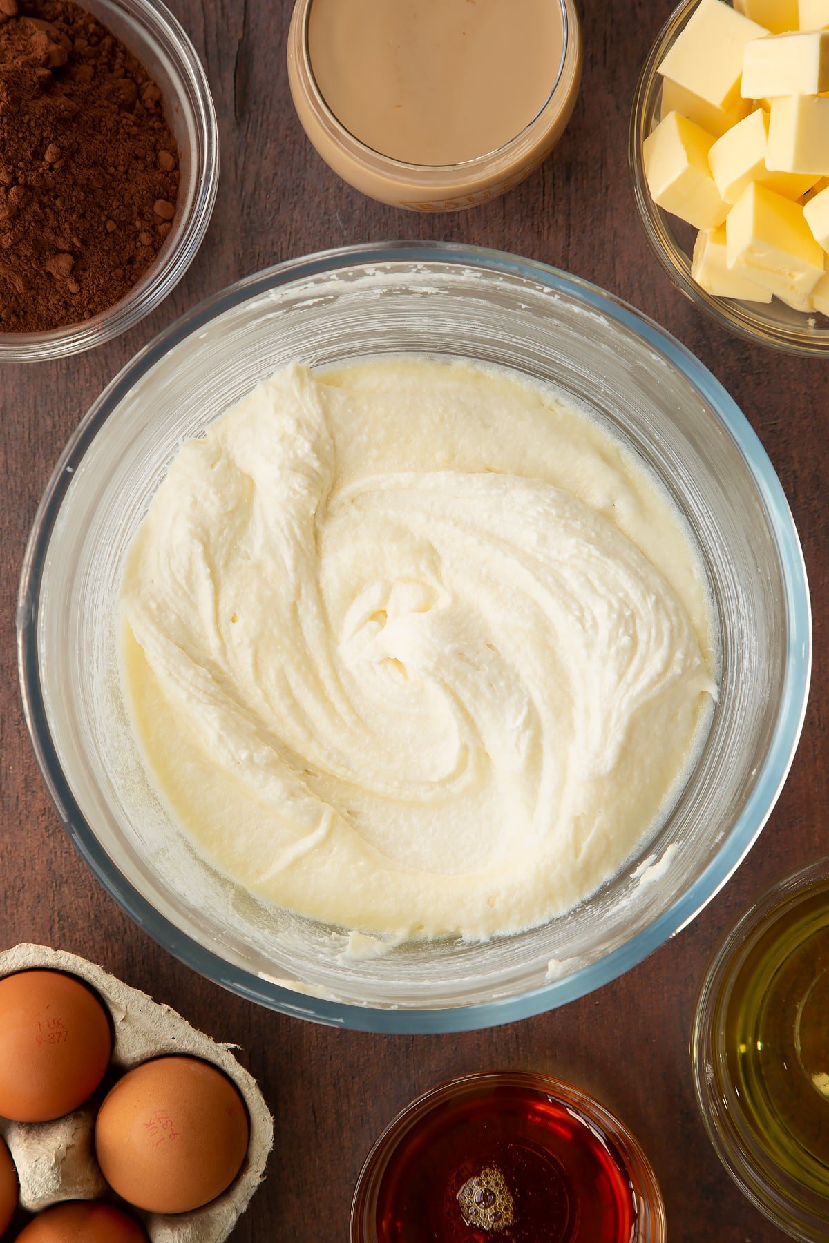 Butter, vegetable oil, caster sugar and golden syrup, whisked together in a glass mixing bowl. Ingredients to make a Baileys cake surround the bowl.