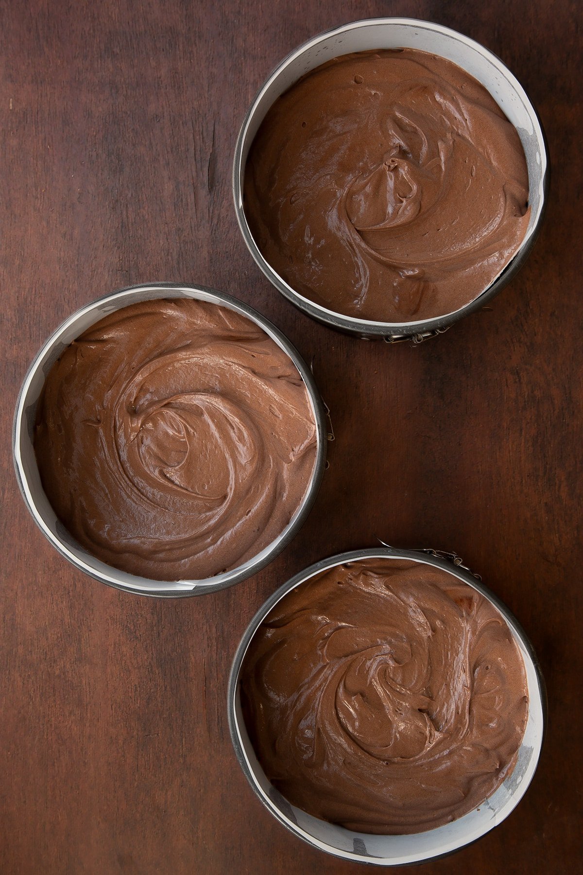 Chocolate Baileys cake batter in three lined cake tins.