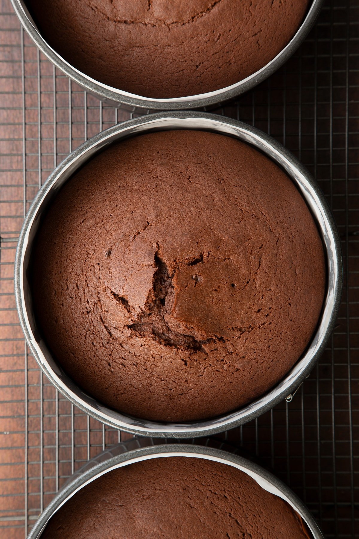 Freshly baked chocolate Baileys cake in three lined tins on a wire cooling rack.