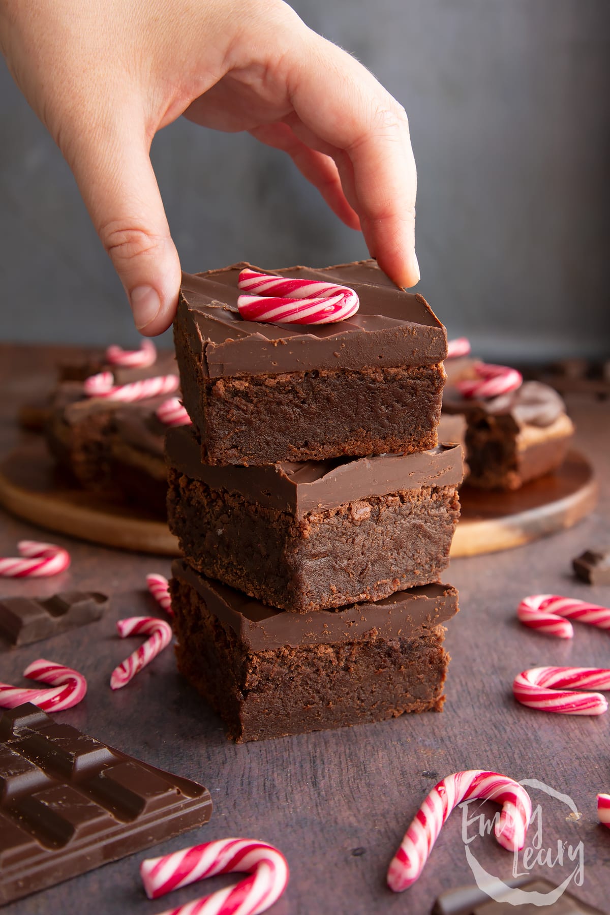 Three candy cane brownies stacked with more in the background. A hand reaches for it.