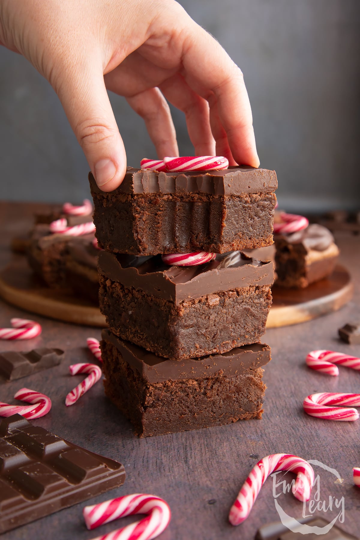 Three candy cane brownies stacked with more in the background. One has a bite out of it and a hand reaches for it.