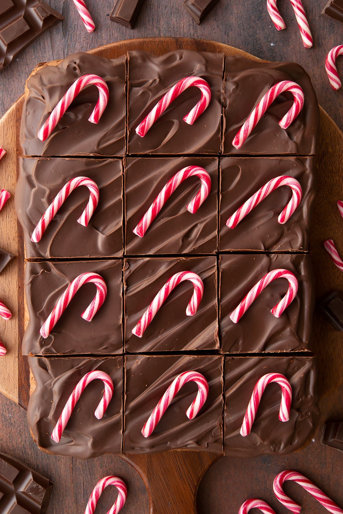 Candy cane brownies on a board, cut into 12 pieces. Each piece has been topped with a candy cane. 