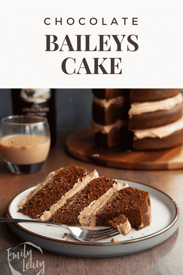 Slice of chocolate Baileys cake with Baileys buttercream frosting on a white plate with a fork. Caption reads: Chocolate Baileys cake.
