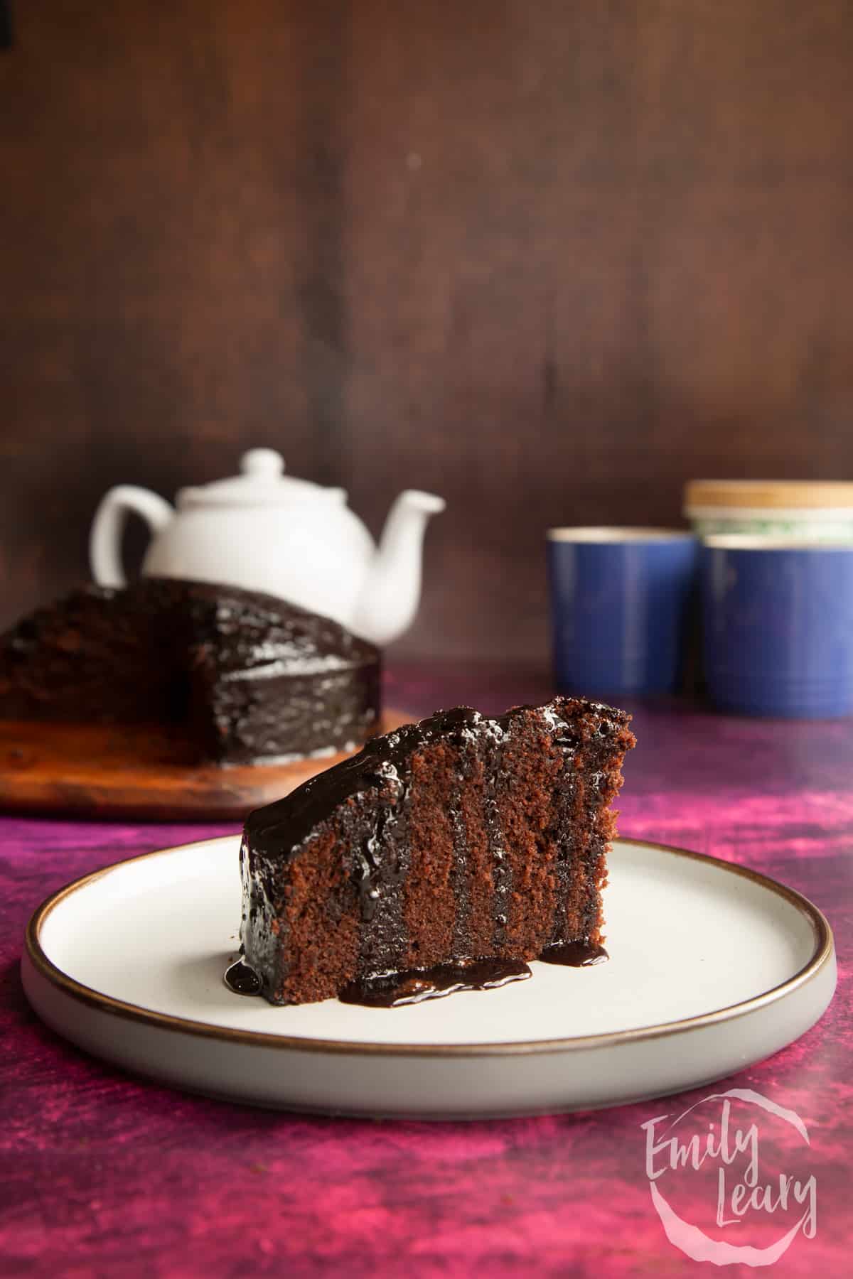 A slice of chocolate drizzle cake on a plate with extra drizzle.