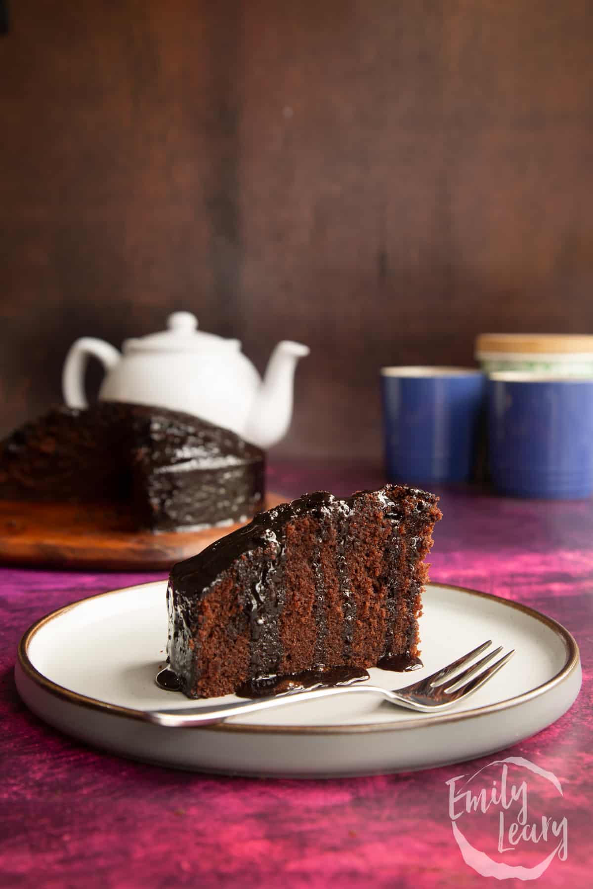 A slice of chocolate drizzle cake on a plate with a fork.