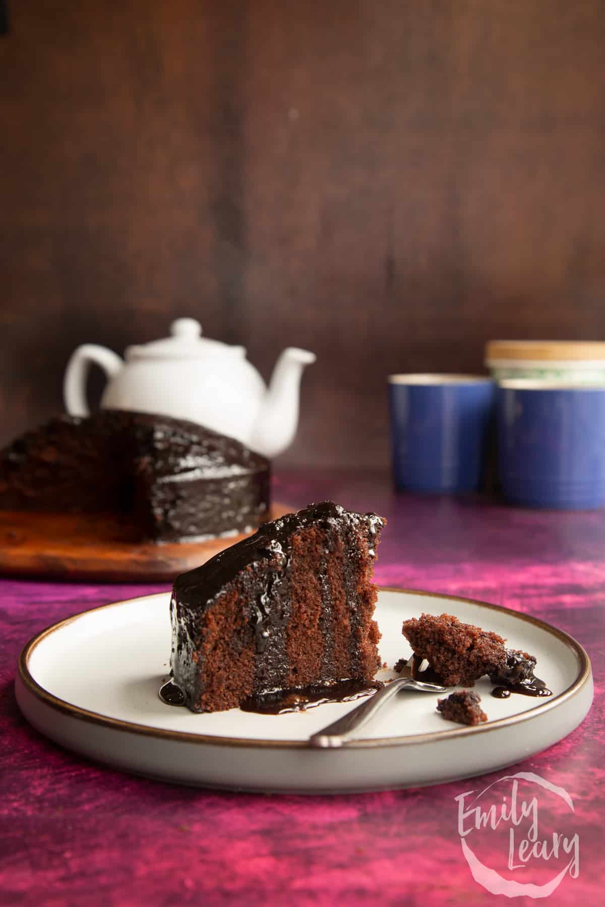 A slice of chocolate drizzle cake on a plate with some crumbs on a fork.