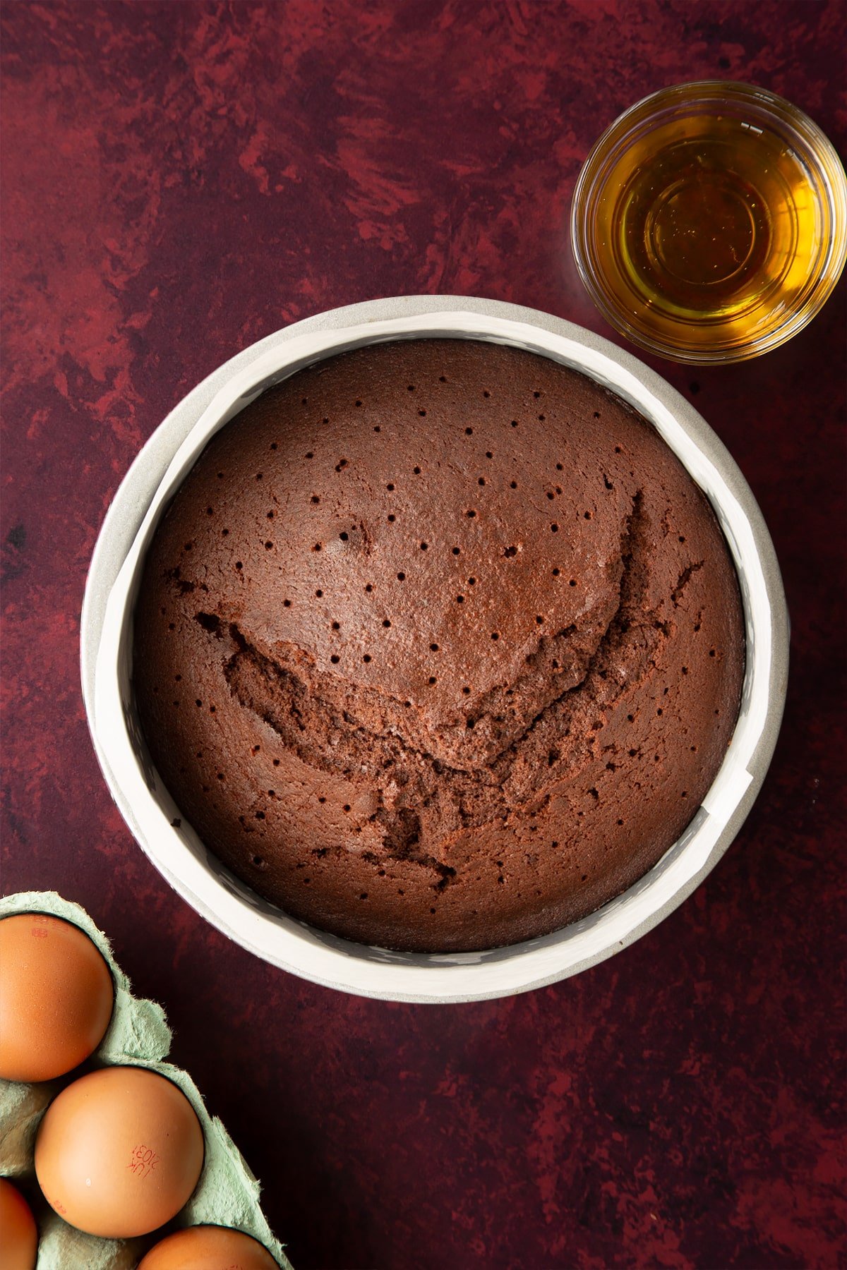 Baked chocolate drizzle cake in a lined tin. It has been pierced all over with a skewer.