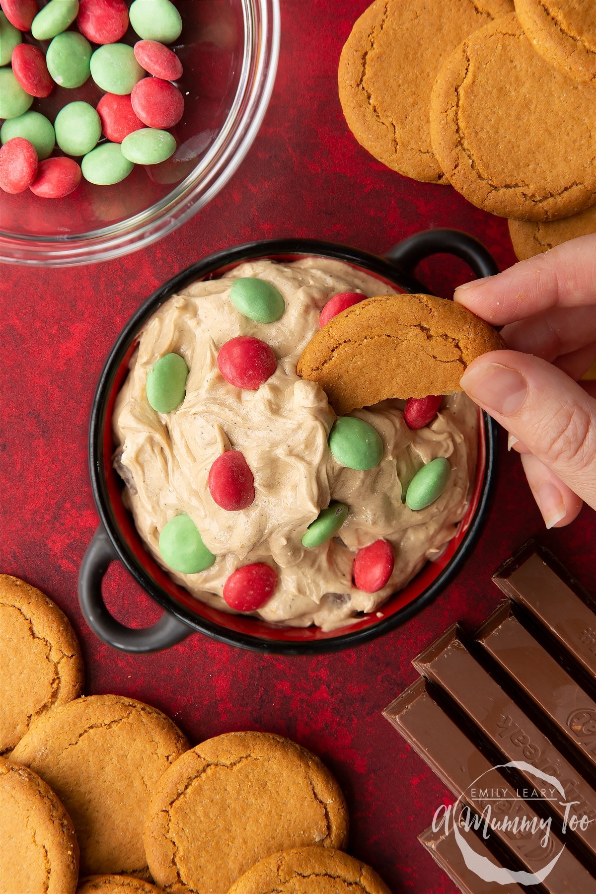 Christmas cookie dip in a black pot. A hand dips a piece of gingernut cookie into the dip. Shown from above.