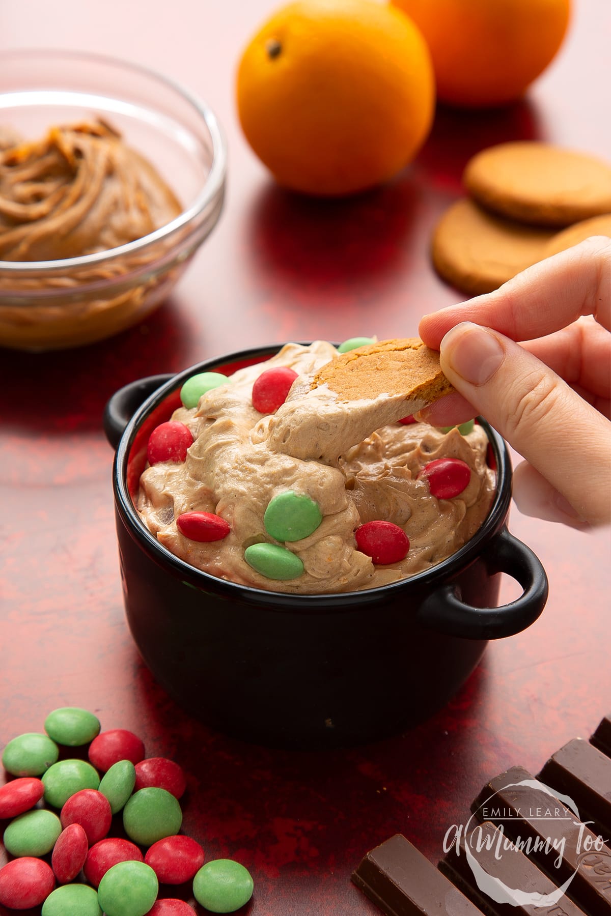 Christmas cookie dip in a black pot. A hand lifts a piece of gingernut cookie out of the dip.