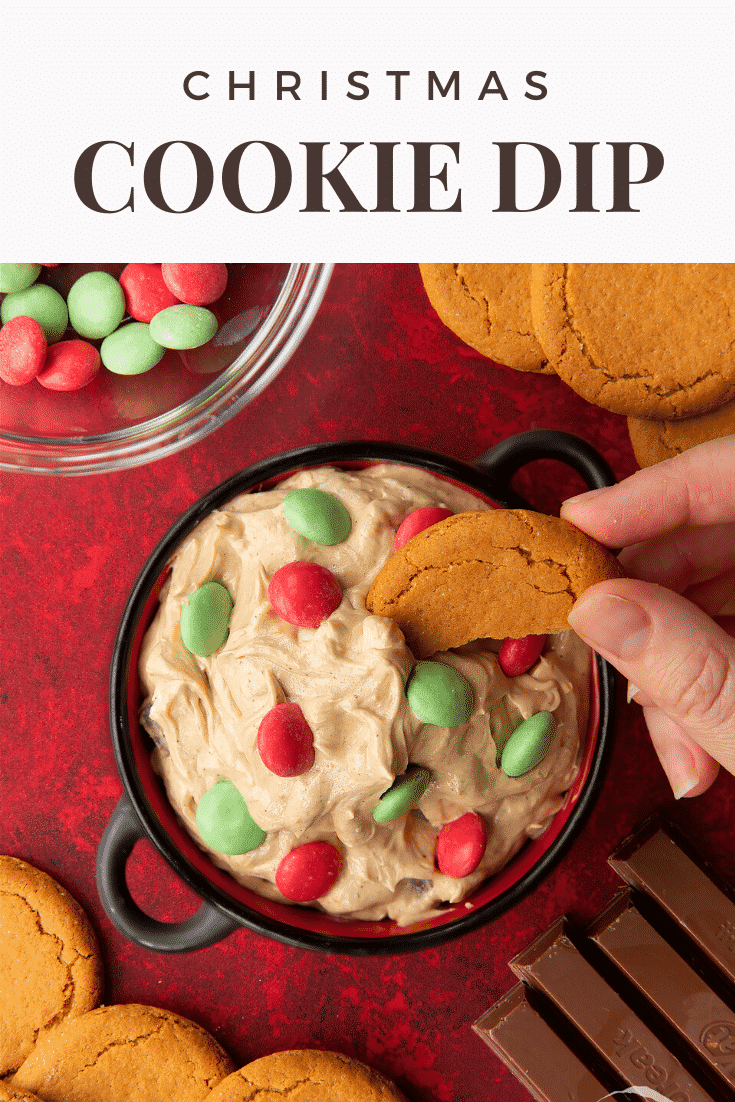 Christmas cookie dip in a black pot. A hand dips a piece of gingernut cookie into the dip. Caption reads: Christmas cookie dip.