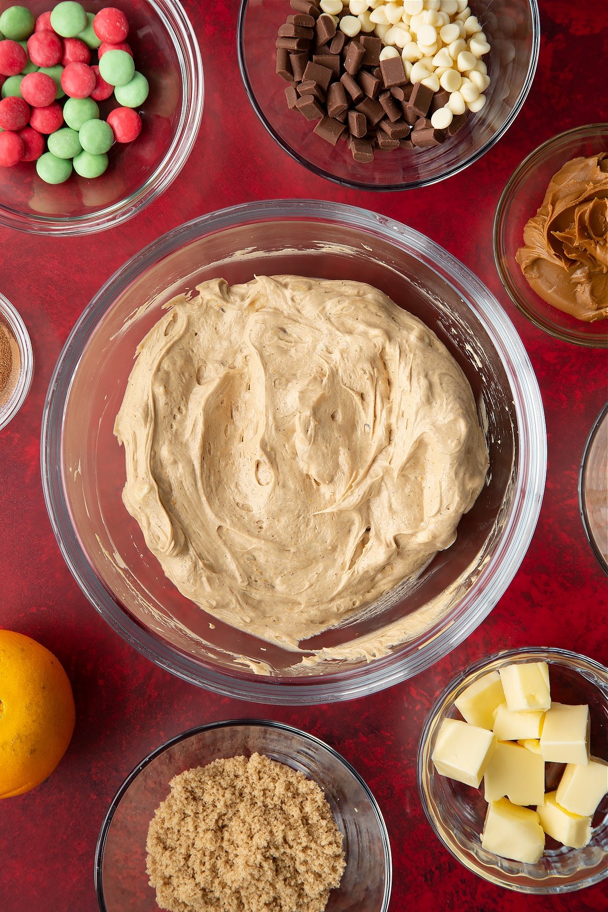 Butter, cream cheese, Biscoff spread, sugar, orange zest and cinnamon, whisked together in a mixing bowl. Ingredients to make Christmas cookie dip surround the bowl.