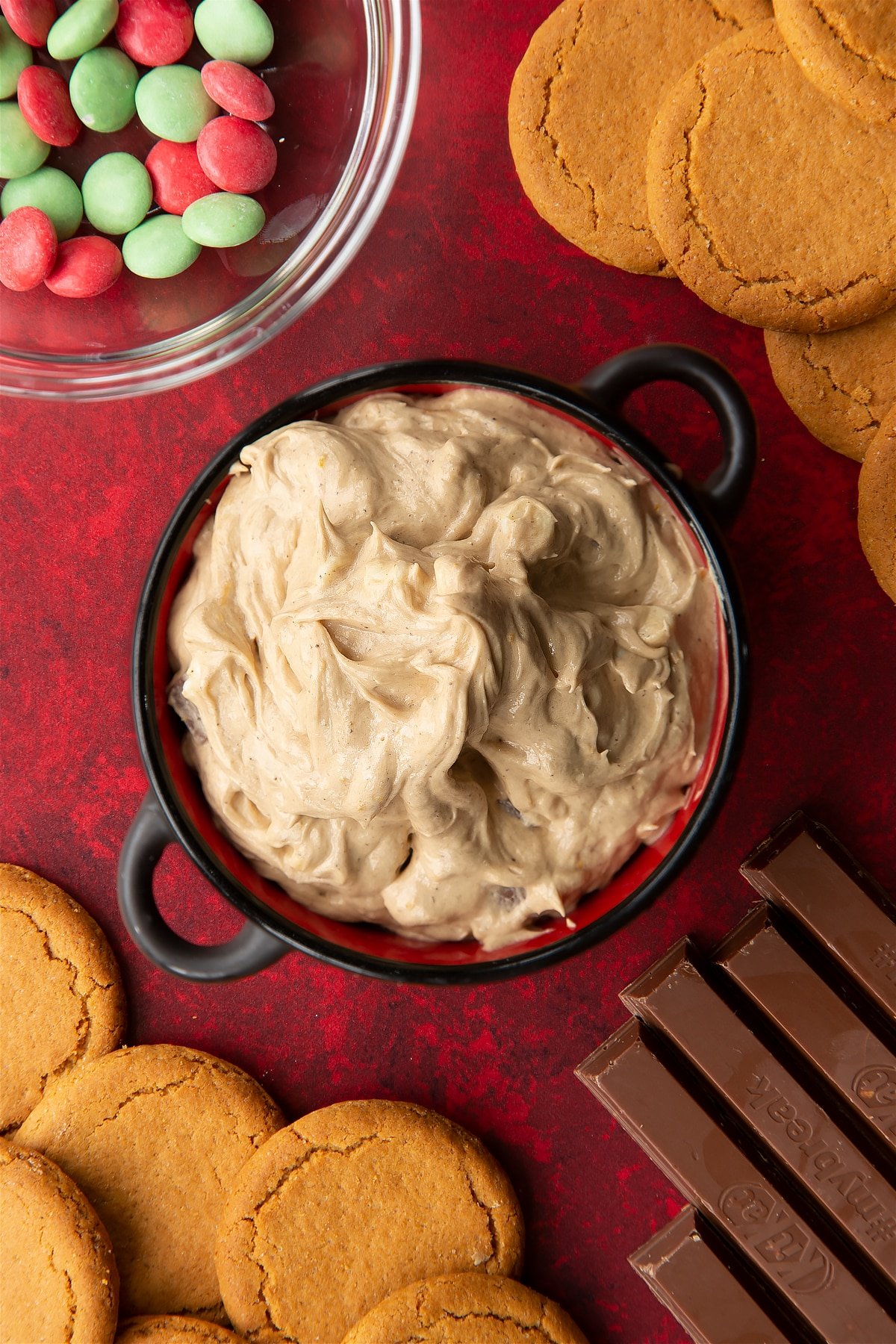 Christmas cookie dip in a black pot. Ingredients to make Christmas cookie dip surround the bowl.