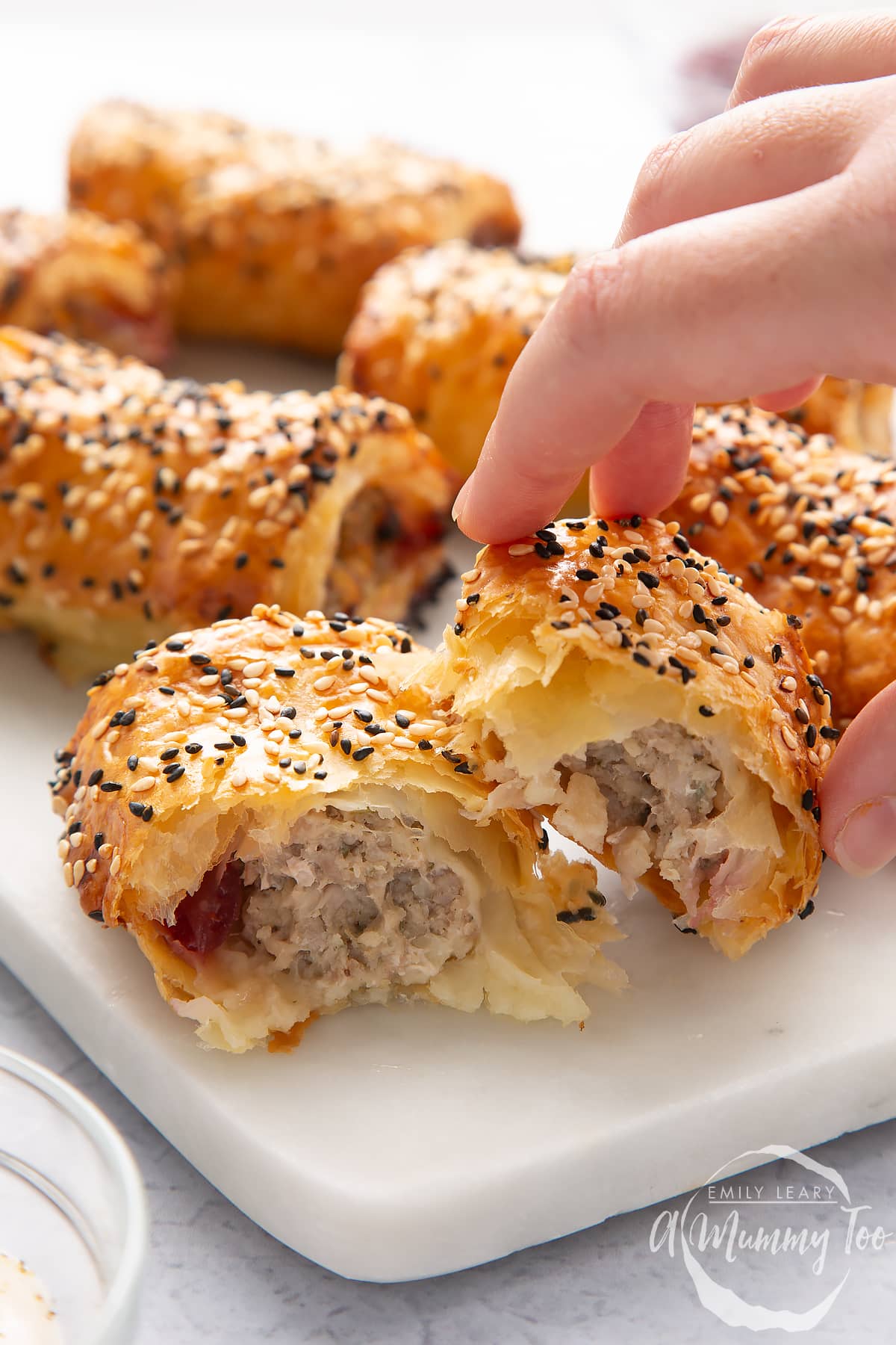 A festive sausage roll broken open on a white marble board. A hand reaches for it.