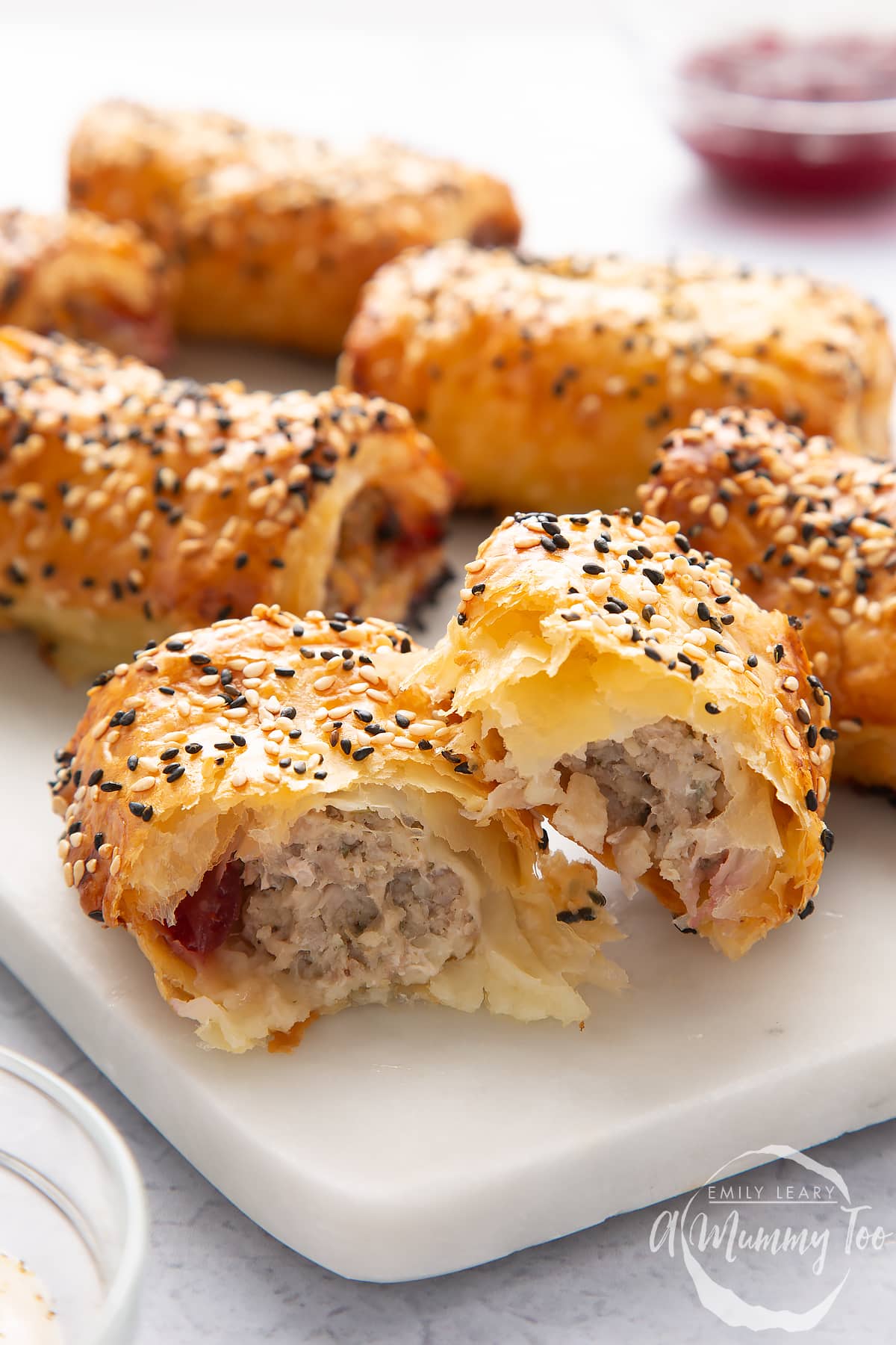 A festive sausage roll broken open on a white marble board, with more in the background.