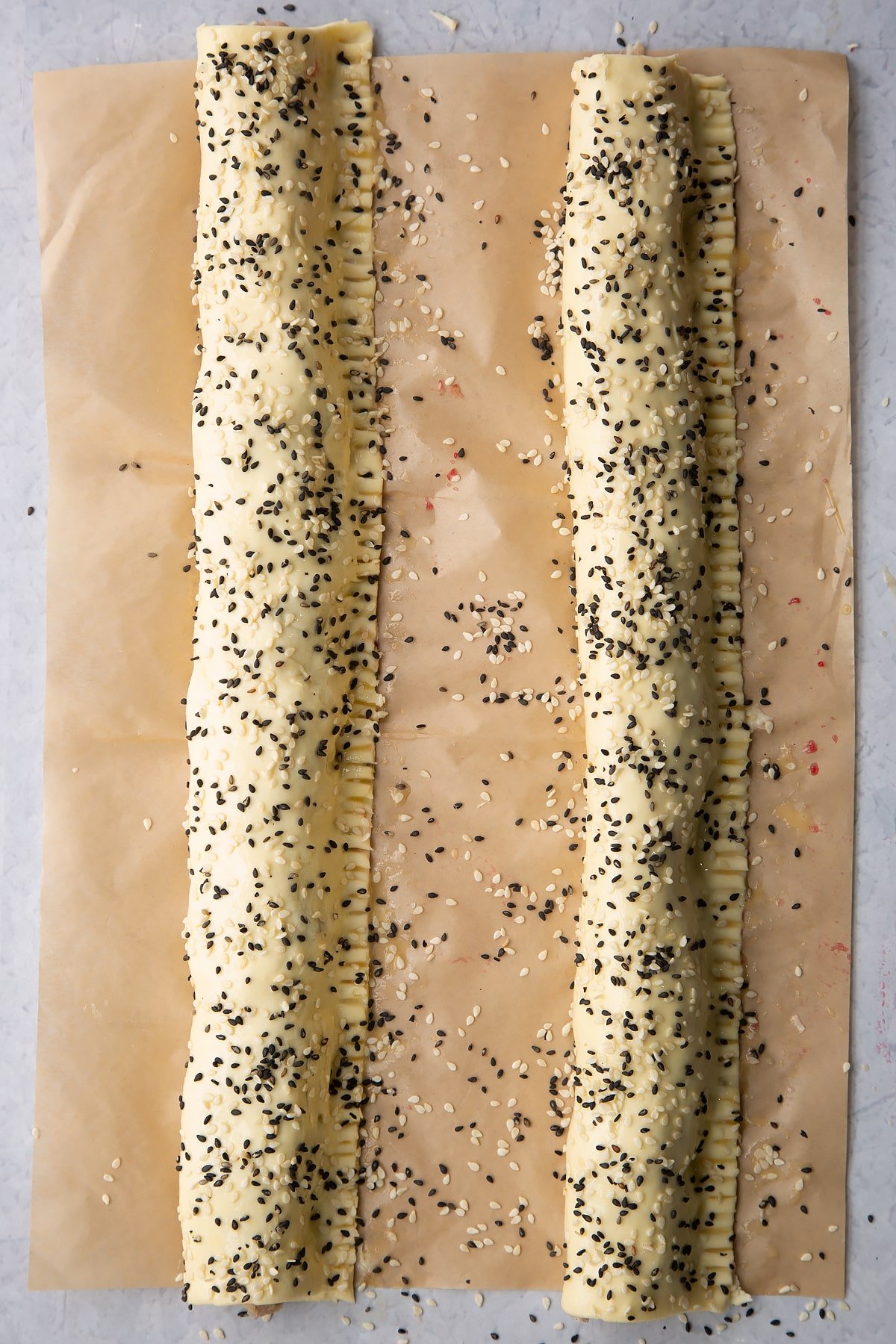 Two lengths of festive sausage meat wrapped in puff pastry , scattered with sesame seeds.