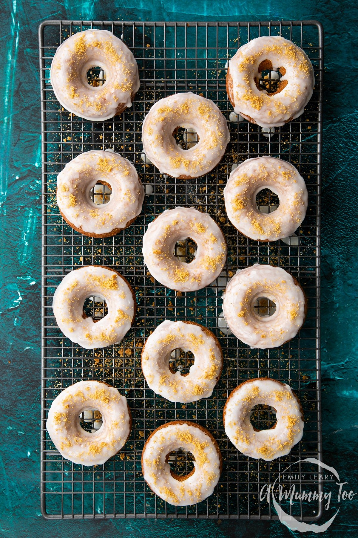 Freshly baked gingerbread donuts on a wire cooling rack. They have been dipped in lemon glaze and sprinkled with crushed gingernut biscuits.