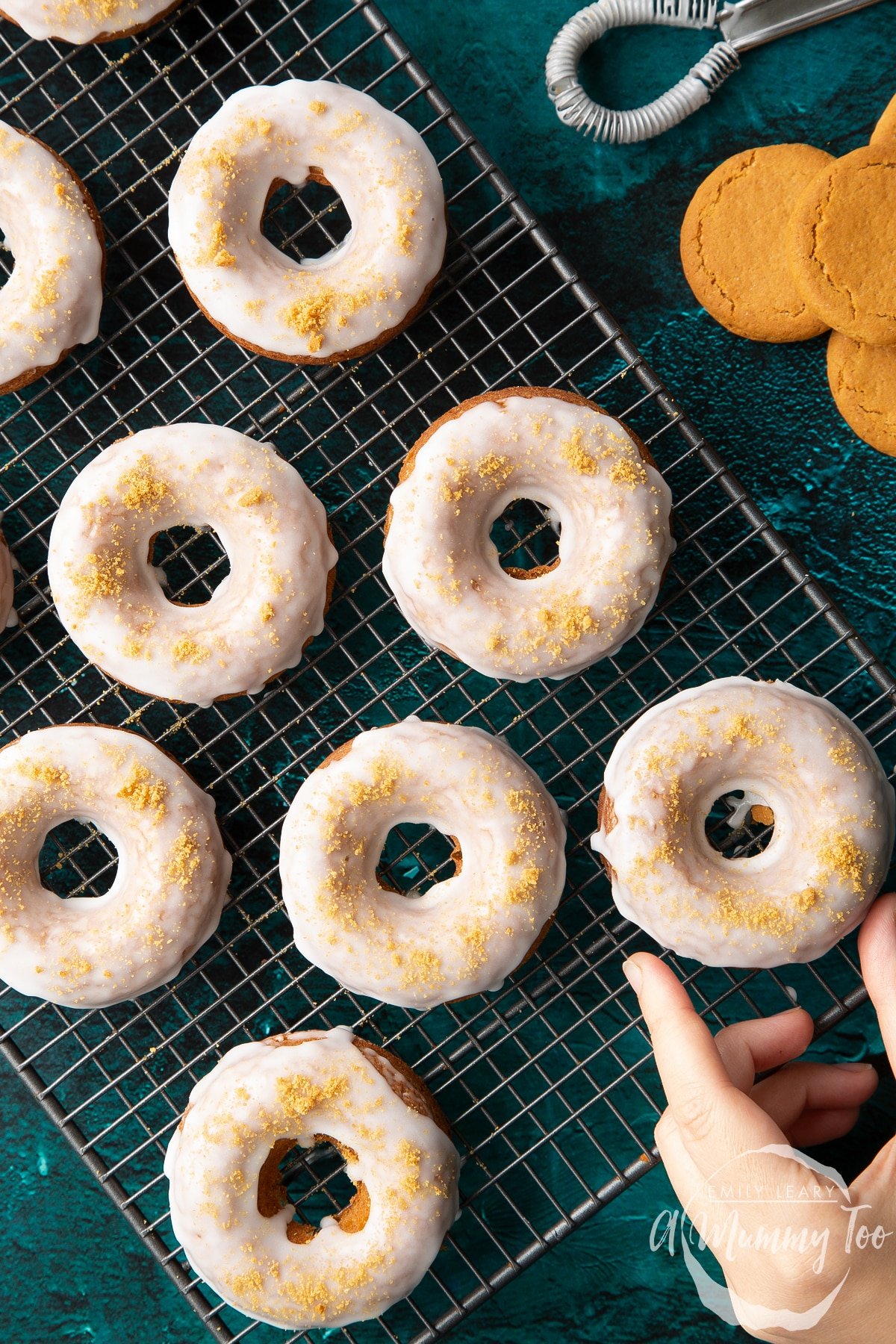 Baked gingerbread donuts with a lemon glaze on a wire cooling rack. A hand reaches for one. Shown from above. 