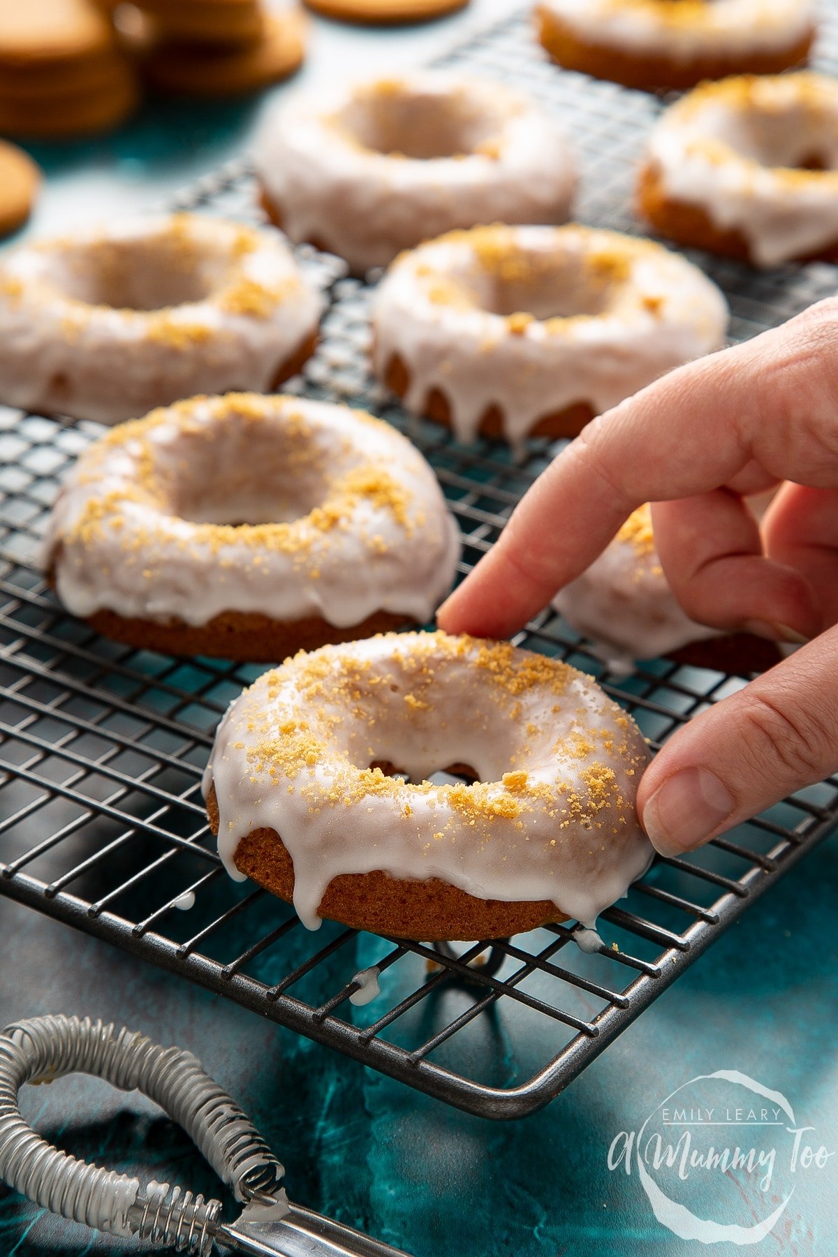 Baked gingerbread donuts with a lemon glaze on a wire cooling rack. A hand reaches for one.