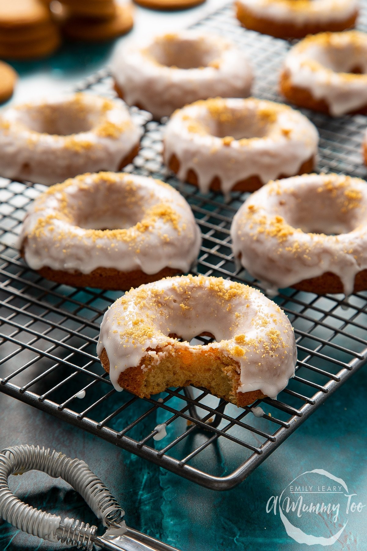 Baked gingerbread donuts with a lemon glaze on a wire cooling rack. One has a bite out of it.