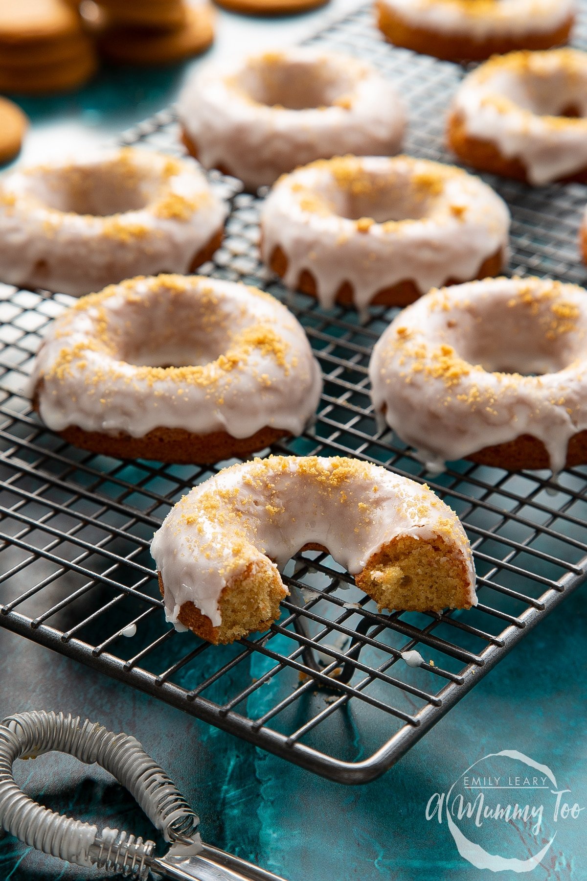 Baked gingerbread donuts with a lemon glaze on a wire cooling rack. One has been part eaten.