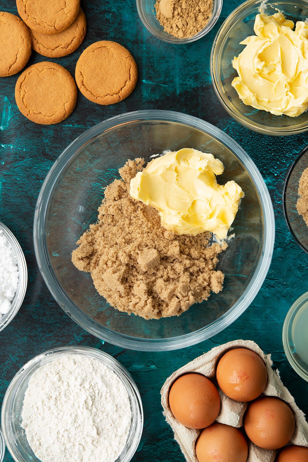 Butter and brown sugar in a glass mixing bowl. Ingredients to make gingerbread donuts surround the bowl.