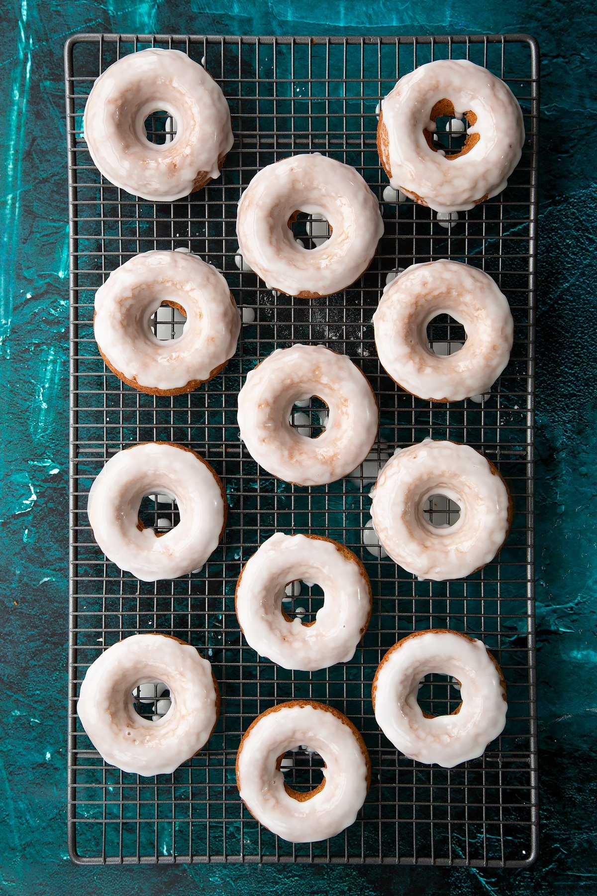 Freshly baked gingerbread donuts on a wire cooling rack. They have been dipped in lemon glaze.