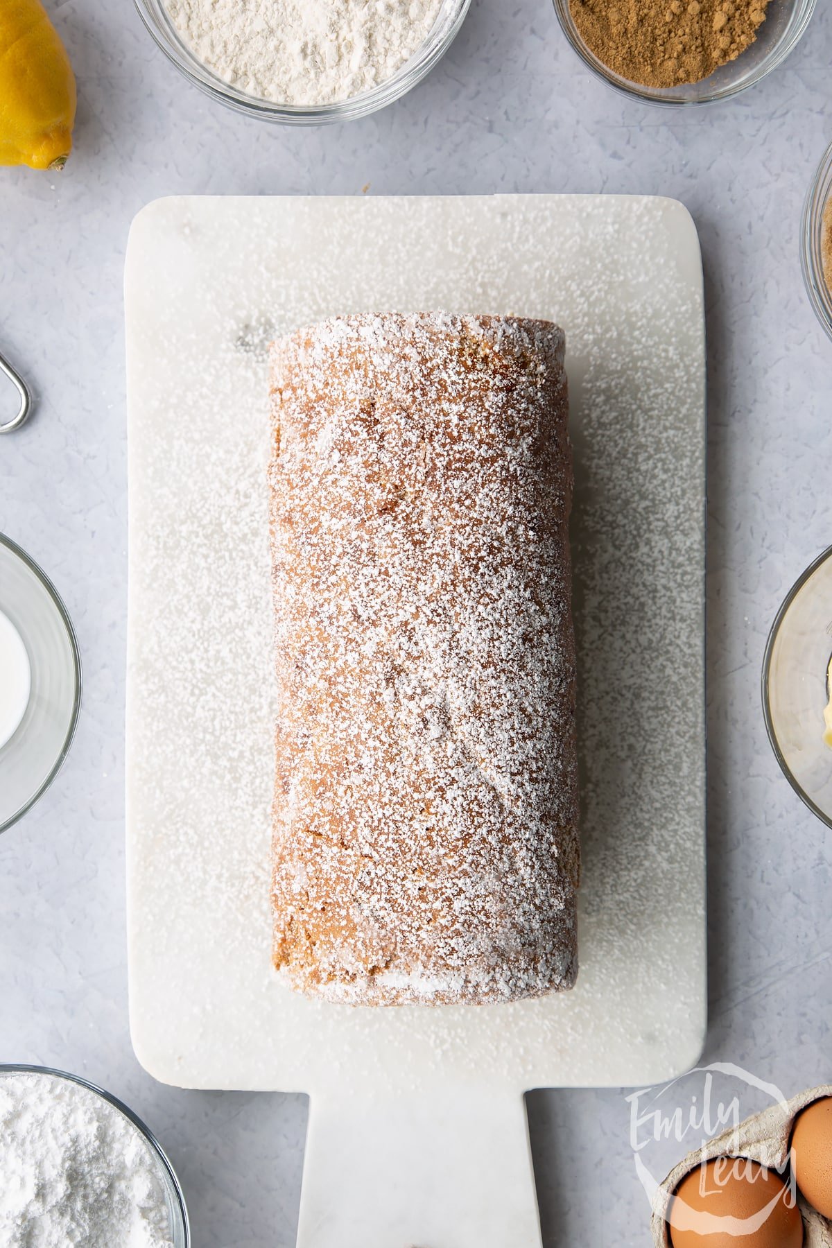 Gingerbread Swiss roll on an icing sugar dusted white marble board.