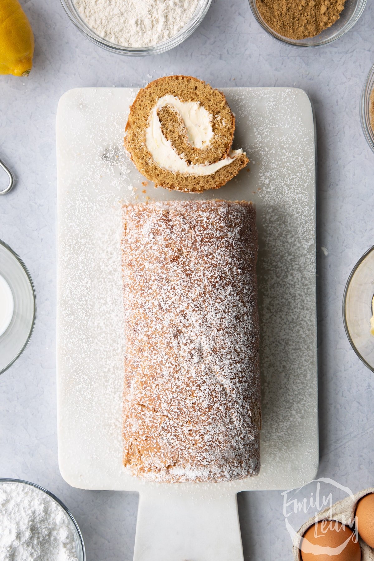 Gingerbread Swiss roll on a white marble board with a slice at the top.