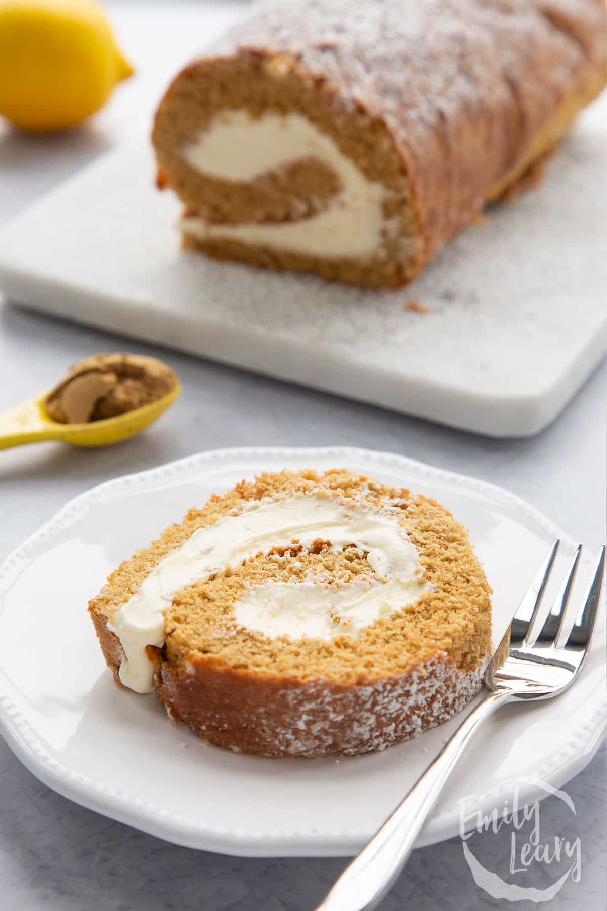 A slice of gingerbread Swiss roll on a white plate with a fork.