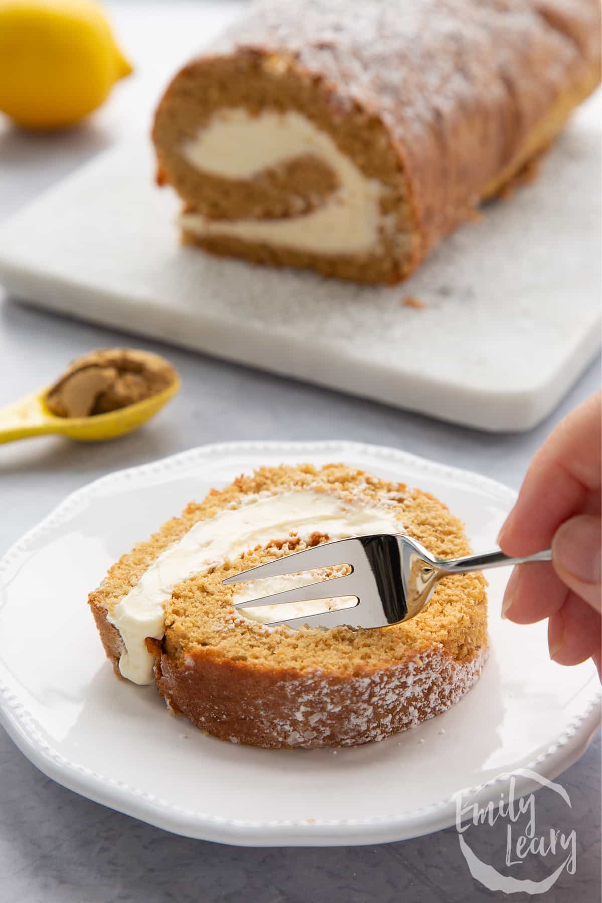 A slice of gingerbread Swiss roll on a white plate with a fork delving in.